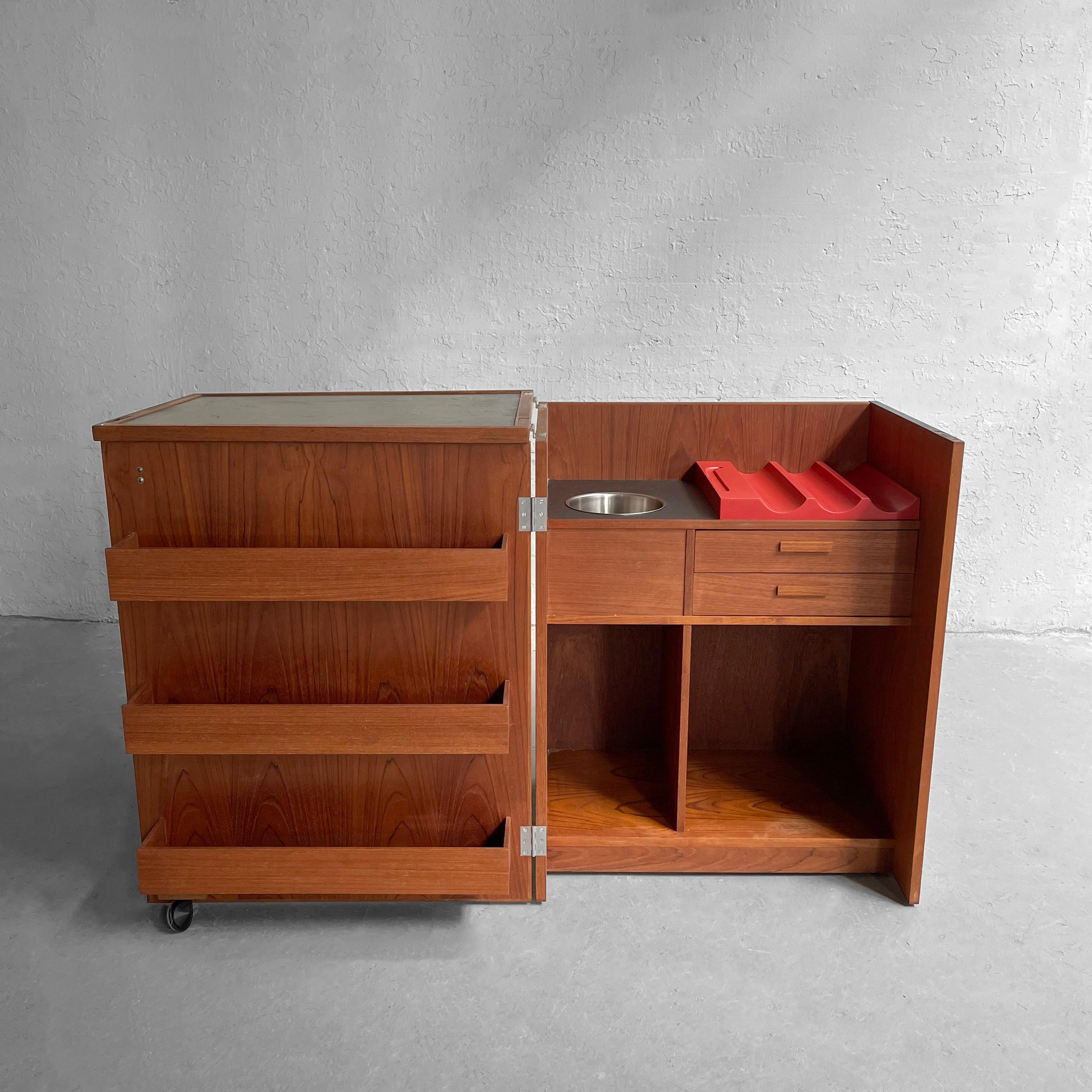 Scandinavian modern, teak, folding bar cabinet designed by Erik Buch for Dyrlund opens into a 48 inch wide, full bar with shelves for glasses, open compartment for liquor bottles, rack for wine bottles, a removeable aluminum ice bucket and a vinyl
