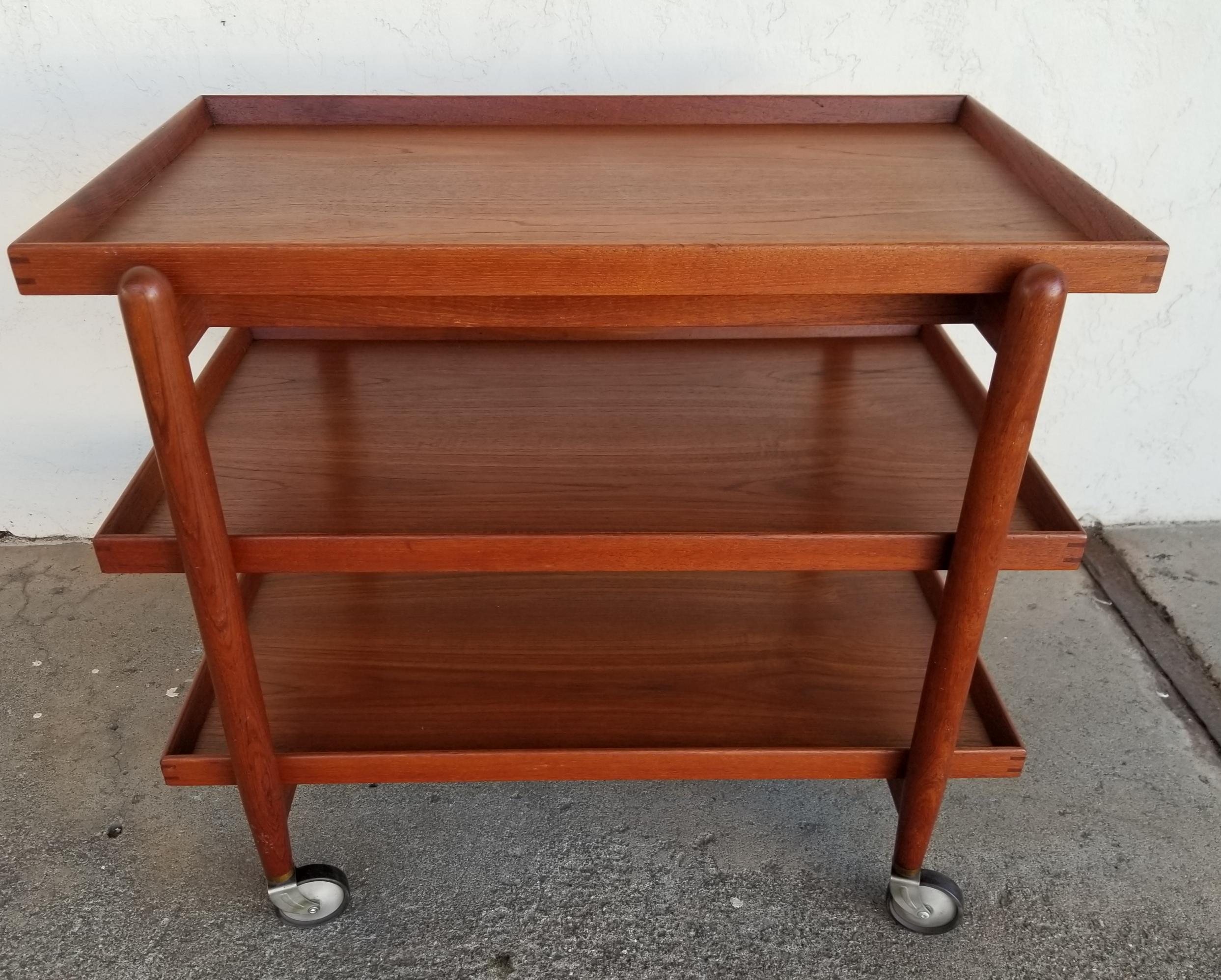 A 3-tier teak Danish modern bar cart / trolley on castors designed by Poul Hundevad, Denmark, circa 1960. Versatile configuration featuring a 3 tray design, 2 removable for serving or 1 may be attached to top level extending work or display surface