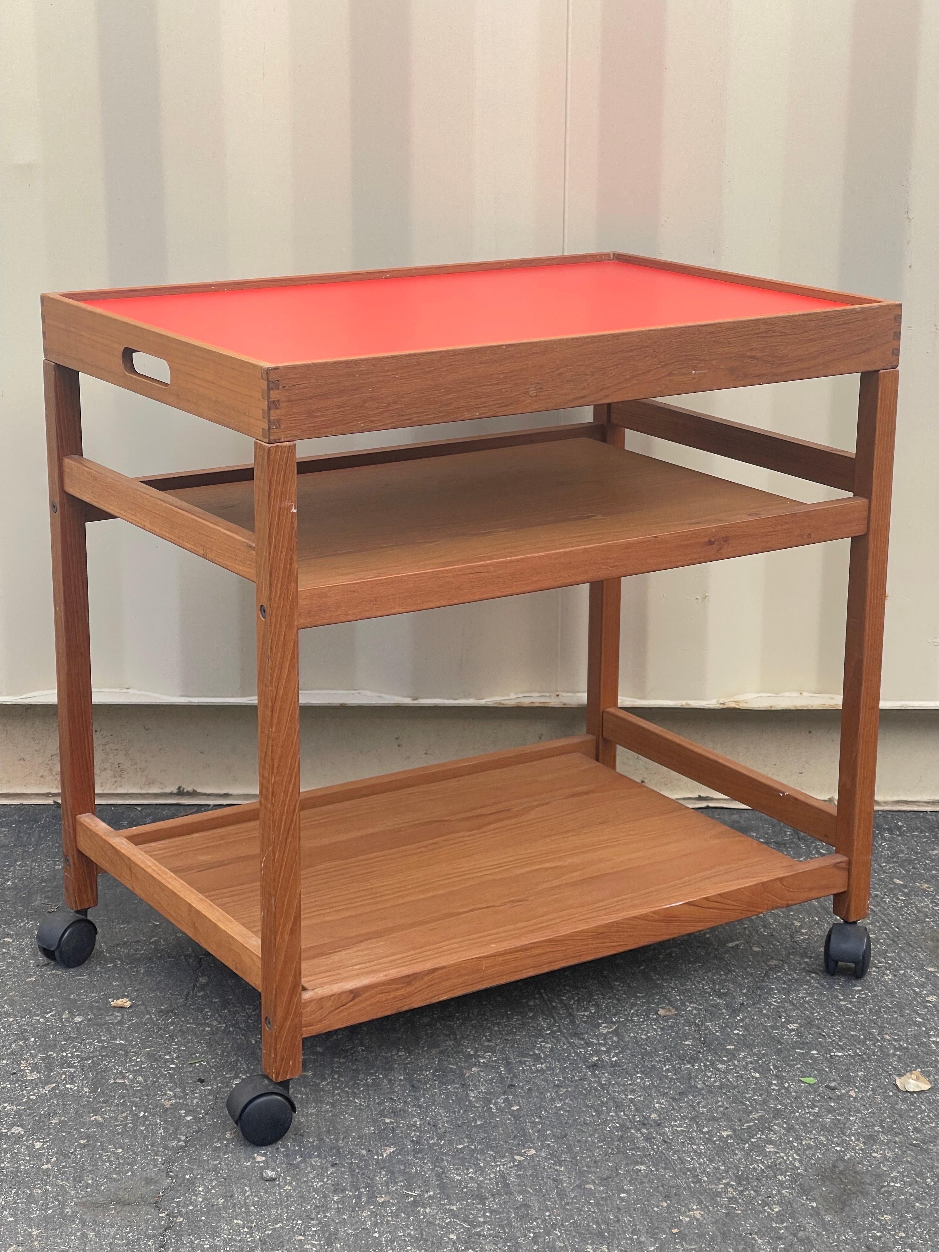Super rare and extremely desirable Danish modern teak bar cart or serving trolley with reversible and removable tray, circa 1970s. The top shelf is removable tray that lifts off; one side has a bright orange laminate surface and the other a black