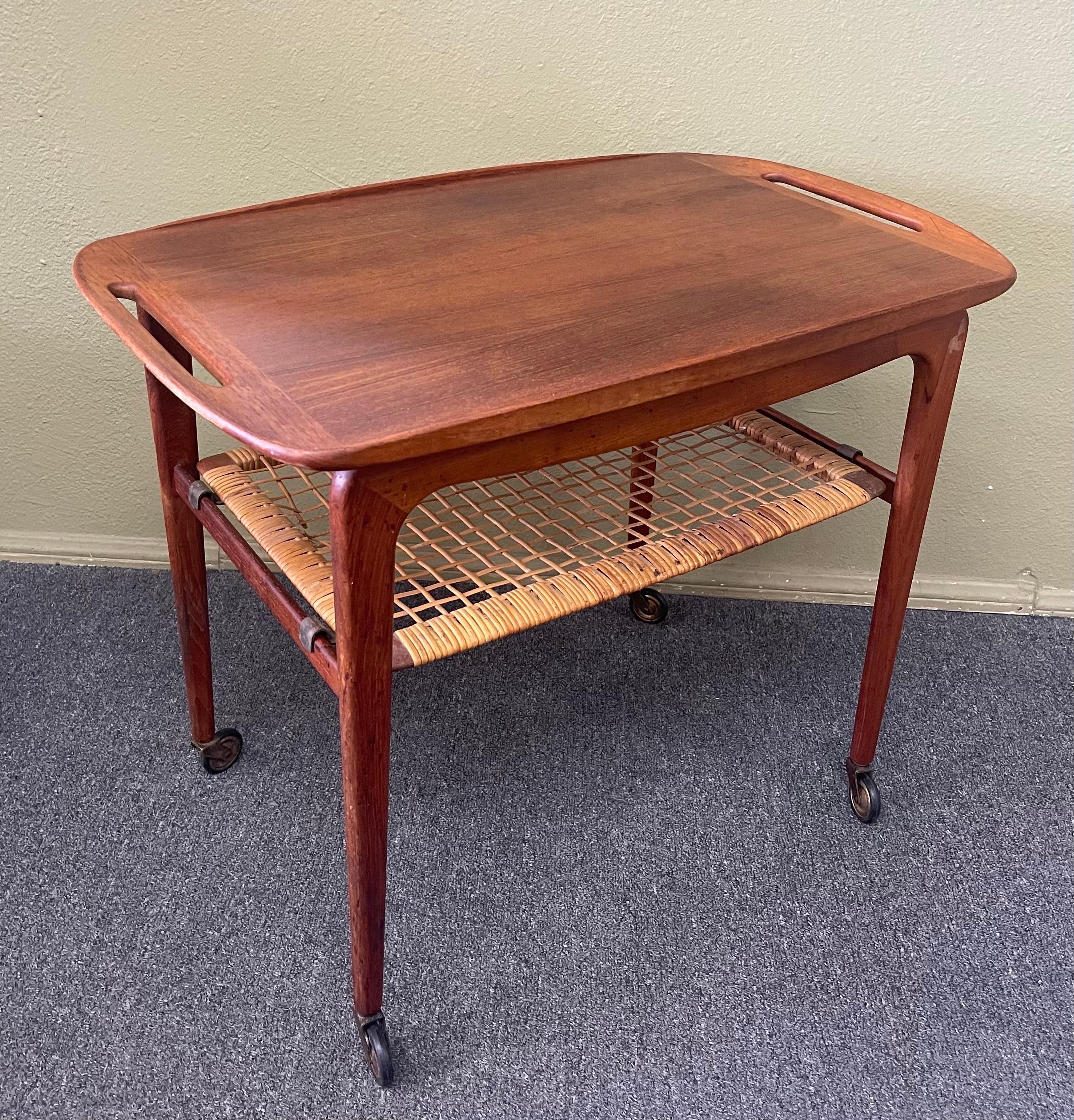 Super rare and extremely desirable Danish modern teak bar cart with removable tray & cane shelf by Johannes Andersen for CFC Silkeborg circa 1950s. The cart has a removable teak shelf with two handles and a lower cane magazine shelf that is also