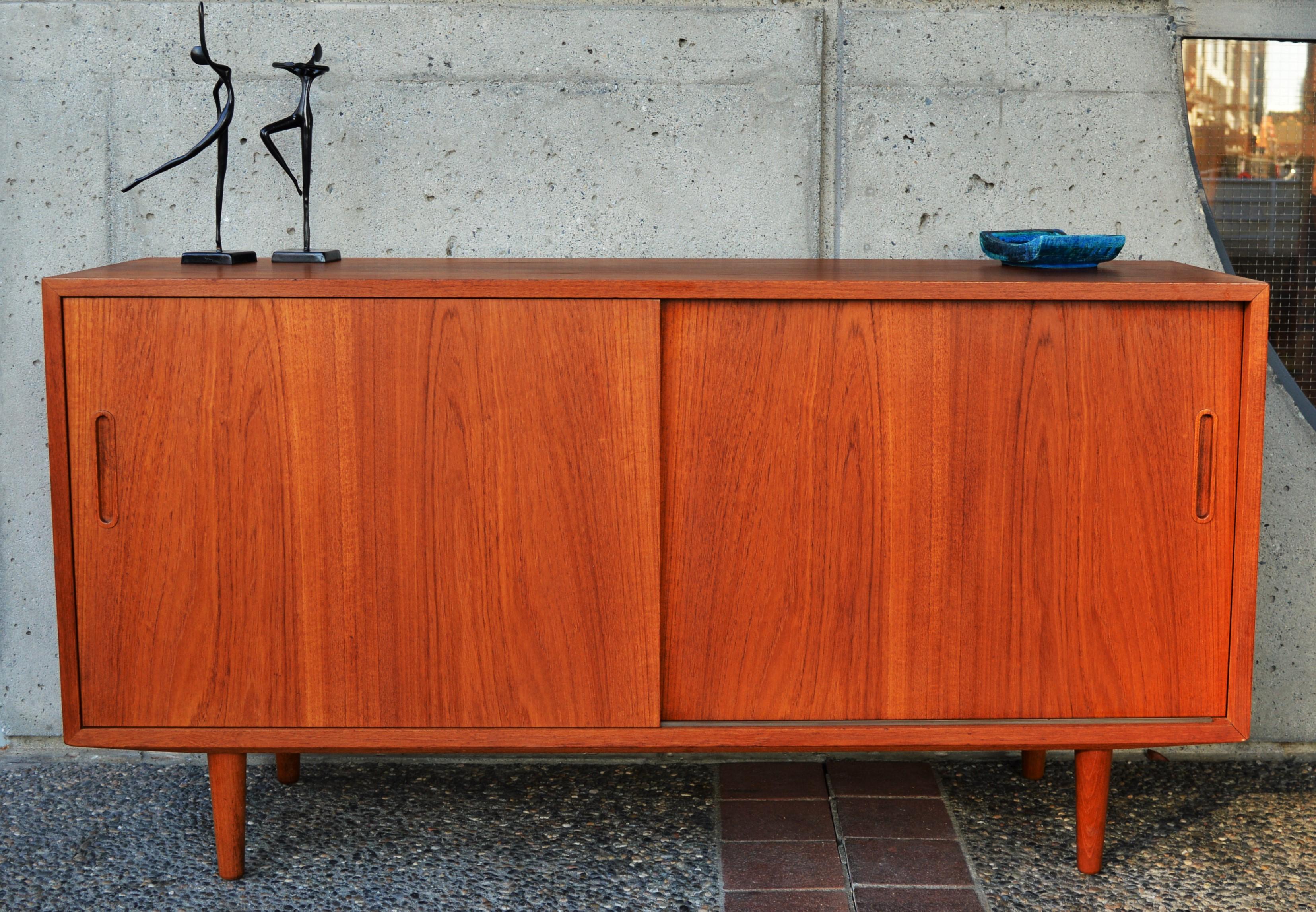 This hot Danish Modern teak compact buffet was designed by Hundevad & Co. in the 1960s and features gorgeous grain - check out those door fronts! - which open to reveal a beech interior with 3 adjustable shelves and one slim profile felted drawer. A