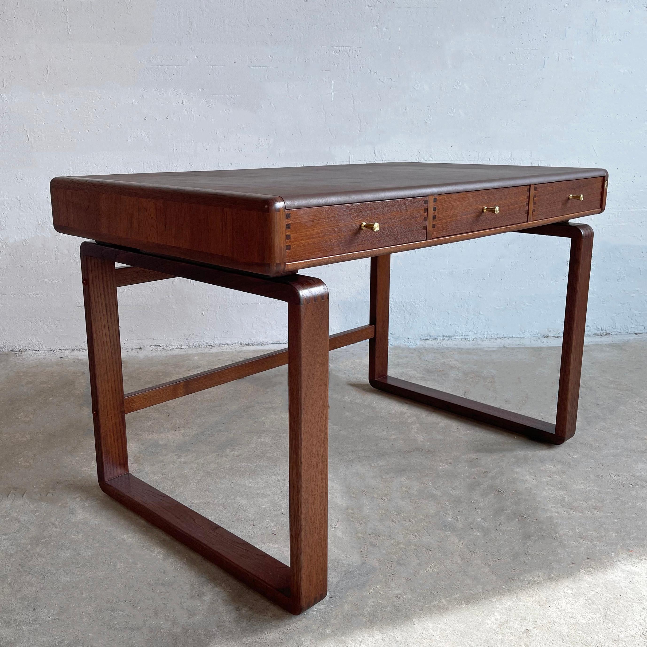 Danish modern, teak desk by D-Scan features a floating top with 3 drawers and a custom brown leather desk surface atop open and airy, bentwood sleigh legs. There are rounded edges throughout with exposed dovetail joinery and brass hardware. The desk