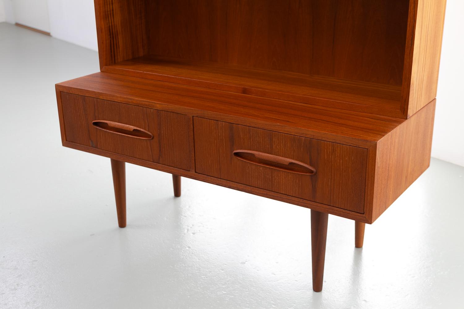 Danish Modern Teak Bookcase, 1960s.

Scandinavian Mid-Century Modern bookcase in teak. Lower part with two wide drawers. Sculpted pulls in solid teak. Upper part has three height adjustable shelves. Depth of shelves 22.5 cm.
Standing on four round