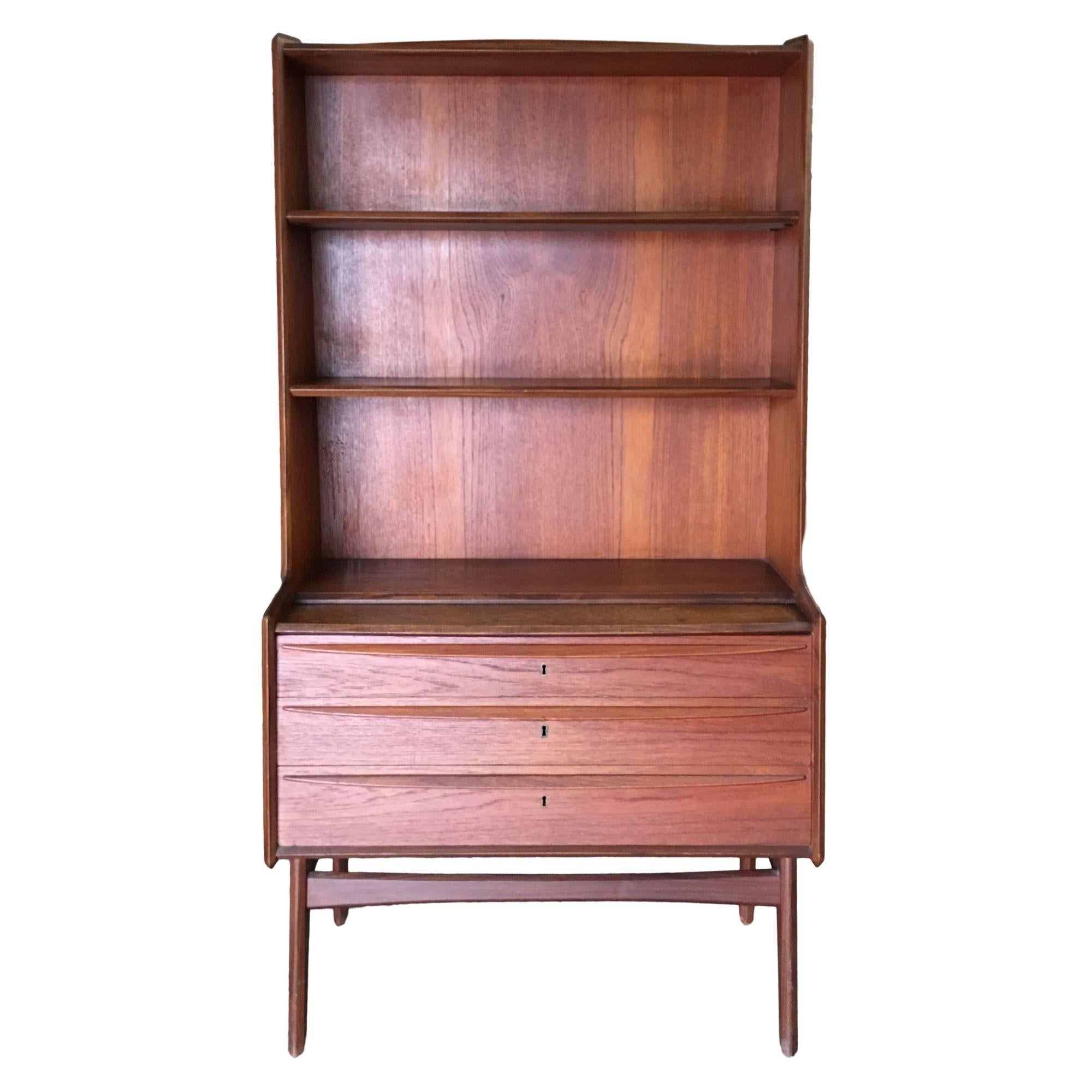 Early 1960s Danish modern teak cupboard display cabinet featuring 3-drawer cabinet with large open fixed 3-shelf display on top all resting a tapered leg base. All 3 drawers featuring bronze skeleton key locks with beautifully sculpted edges along