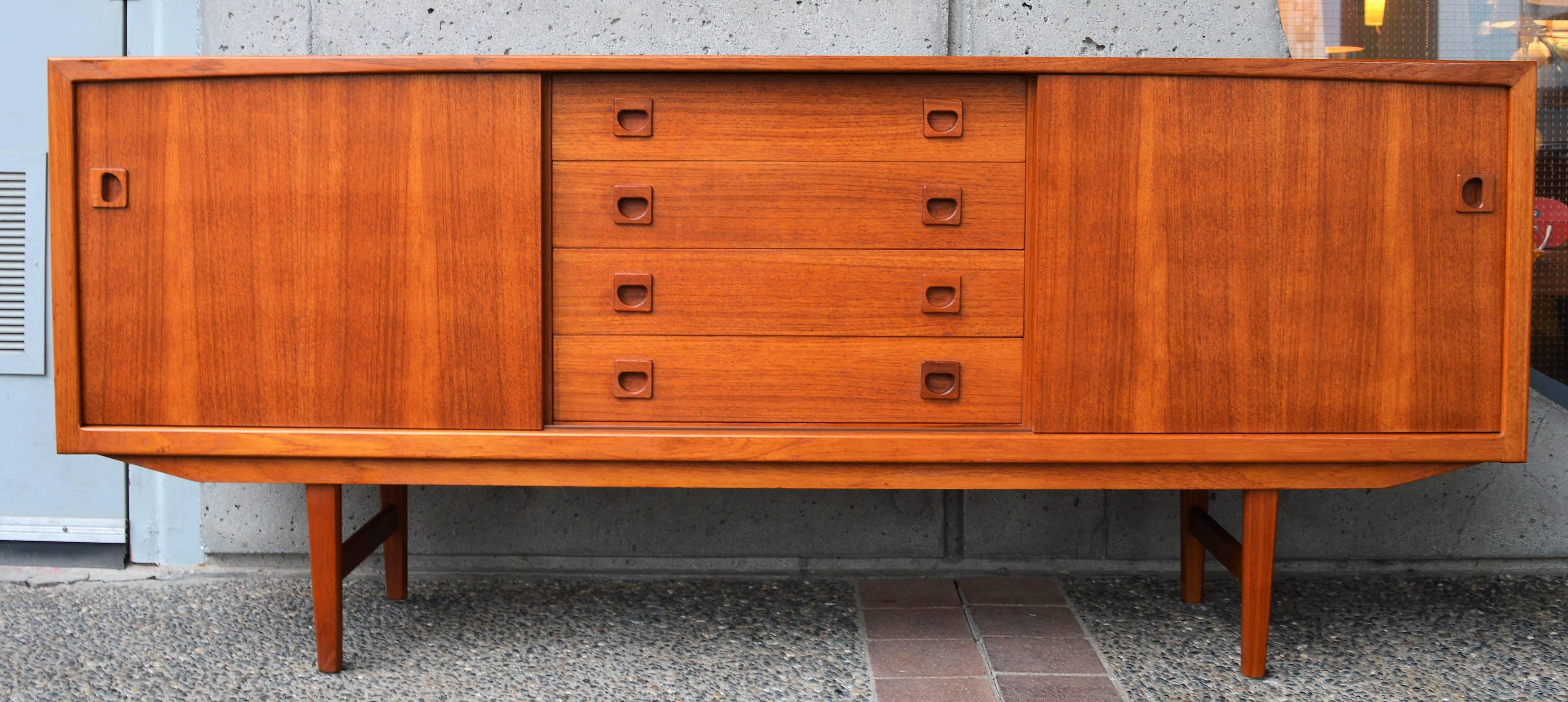 This gorgeous Danish modern teak buffet/credenza has awesome styling. Featuring a sweet front edge molding at the top, which arcs and tapers towards the middle - an Atomic Era style reference to the old TV screens. The center is a bank of four