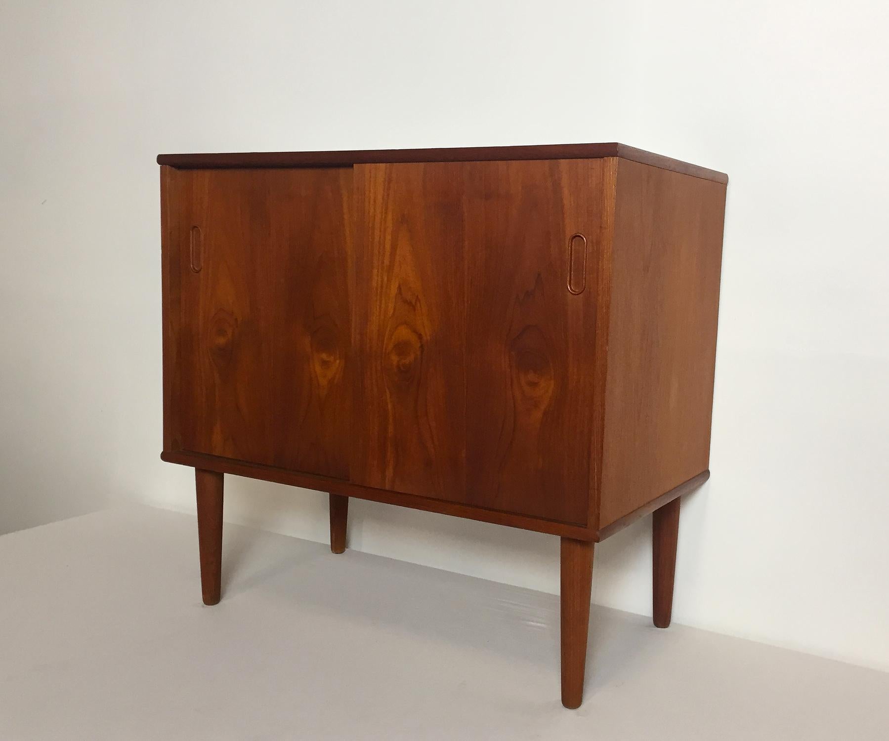 Danish cabinet made of veneered teak wood, 1960s. Front with two sliding doors and a single shelf inside. Tapered massive teak legs with brass detail.
Good condition. Signs of wear consistent with age and use.

Dimensions: 
Height 74.5 cm
Width