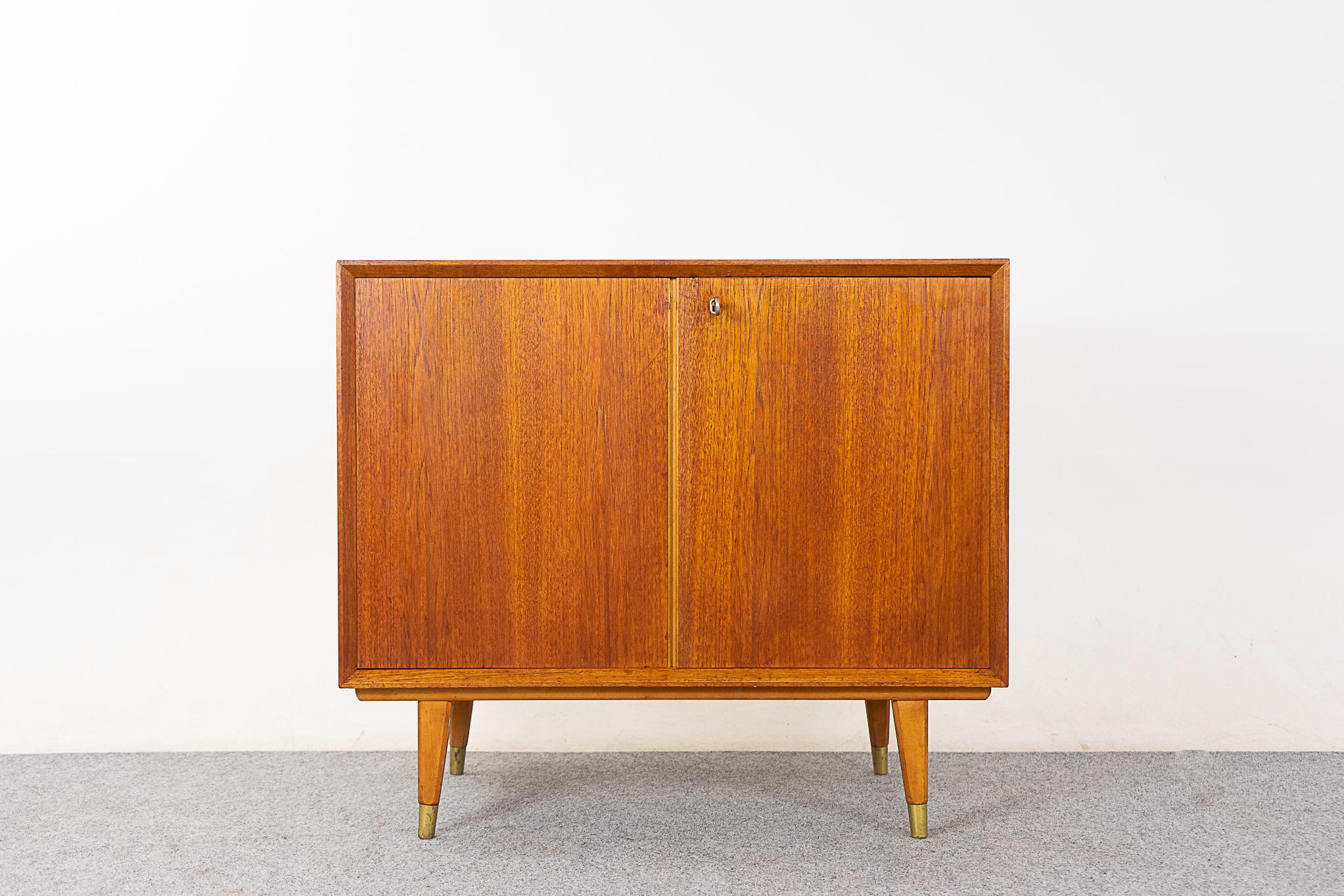 Teak mid-century cabinet, circa 1960's. Clean, simple lined design with beveled front edges and book-matched veneer throughout. Lockable doors, metal capped slender legs, sleek drawer and a fixed height shelf.  

Please inquire for remote and