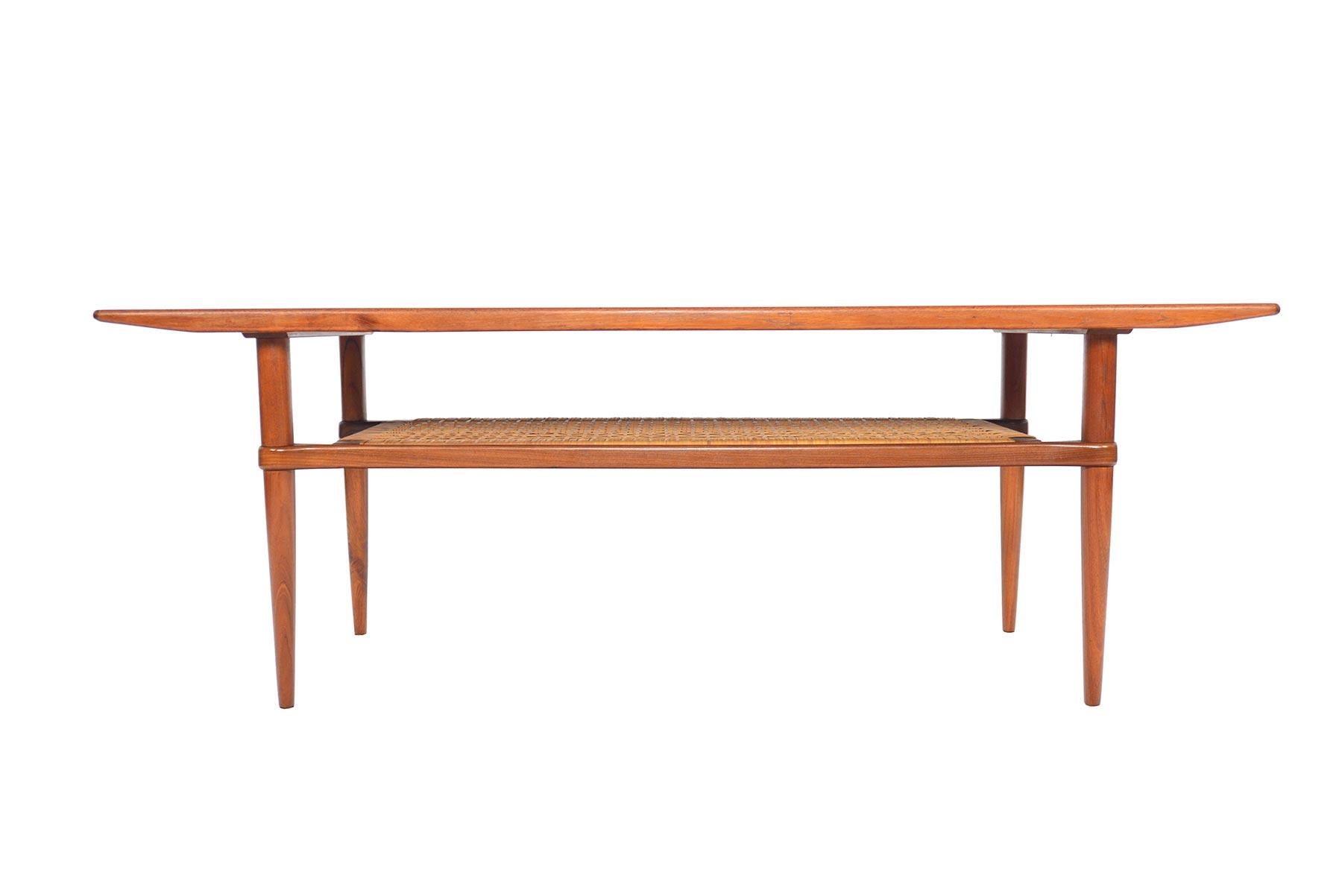 Clean lines and impeccable construction define this stunning Danish modern coffee table. Crafted in teak, this surfboard coffee table features an original caned rack below. Refinished and in excellent condition. 

 