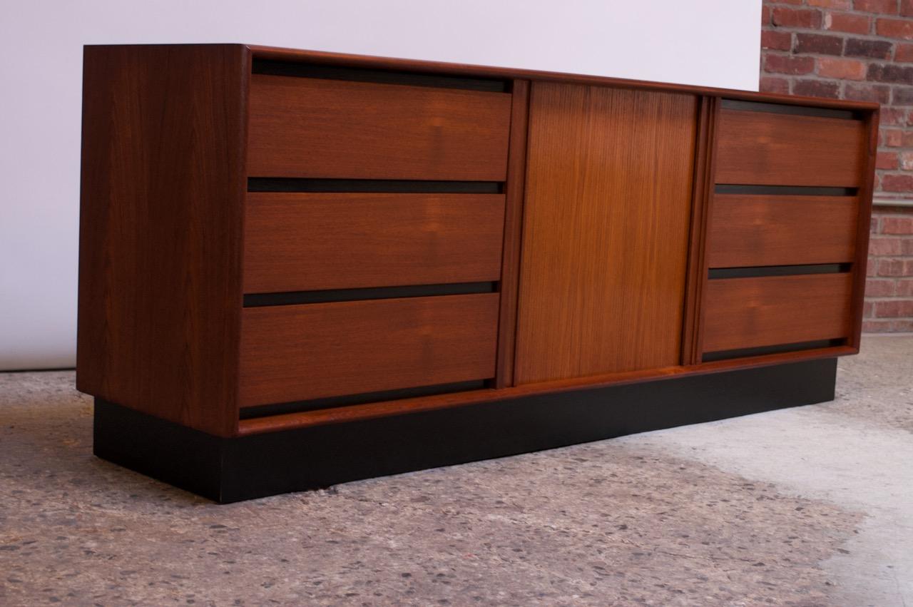 Danish modern chest of drawers / credenza in teak supported by an ebonized plinth base designed by Art Furn and manufactured by Danflex Systems (Denmark, 1960s). Center tambour door, flanked by three drawers on each side, conceals a single,