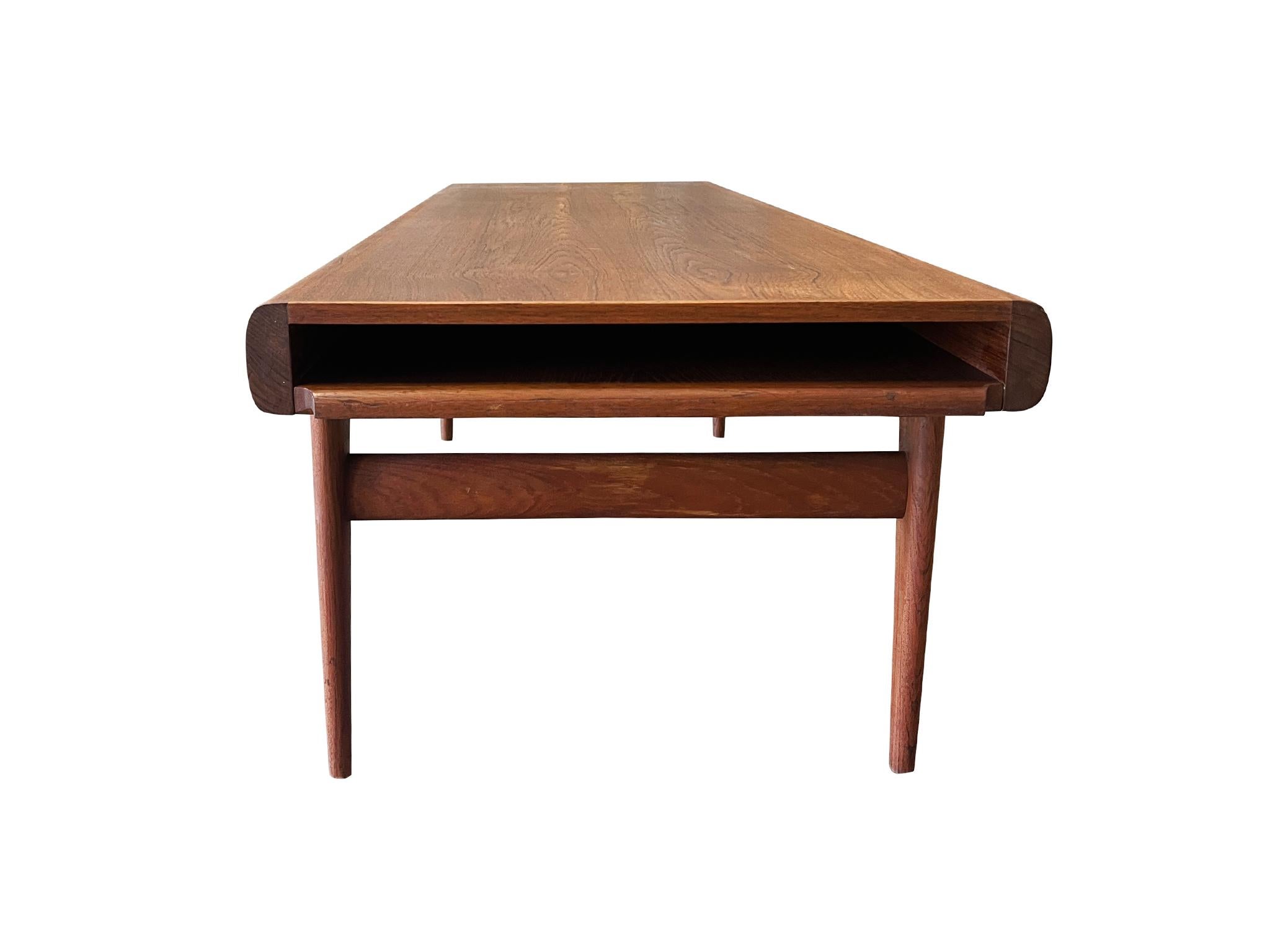 Esta mesa de centro de estilo moderno danés de los años 60 fue diseñada por Johannes Andersen para Uldum Møbelfabrik. Es de teca con un cálido tono marrón rojizo y un rico veteado. De construcción elegante, la mesa se caracteriza por sus bordes