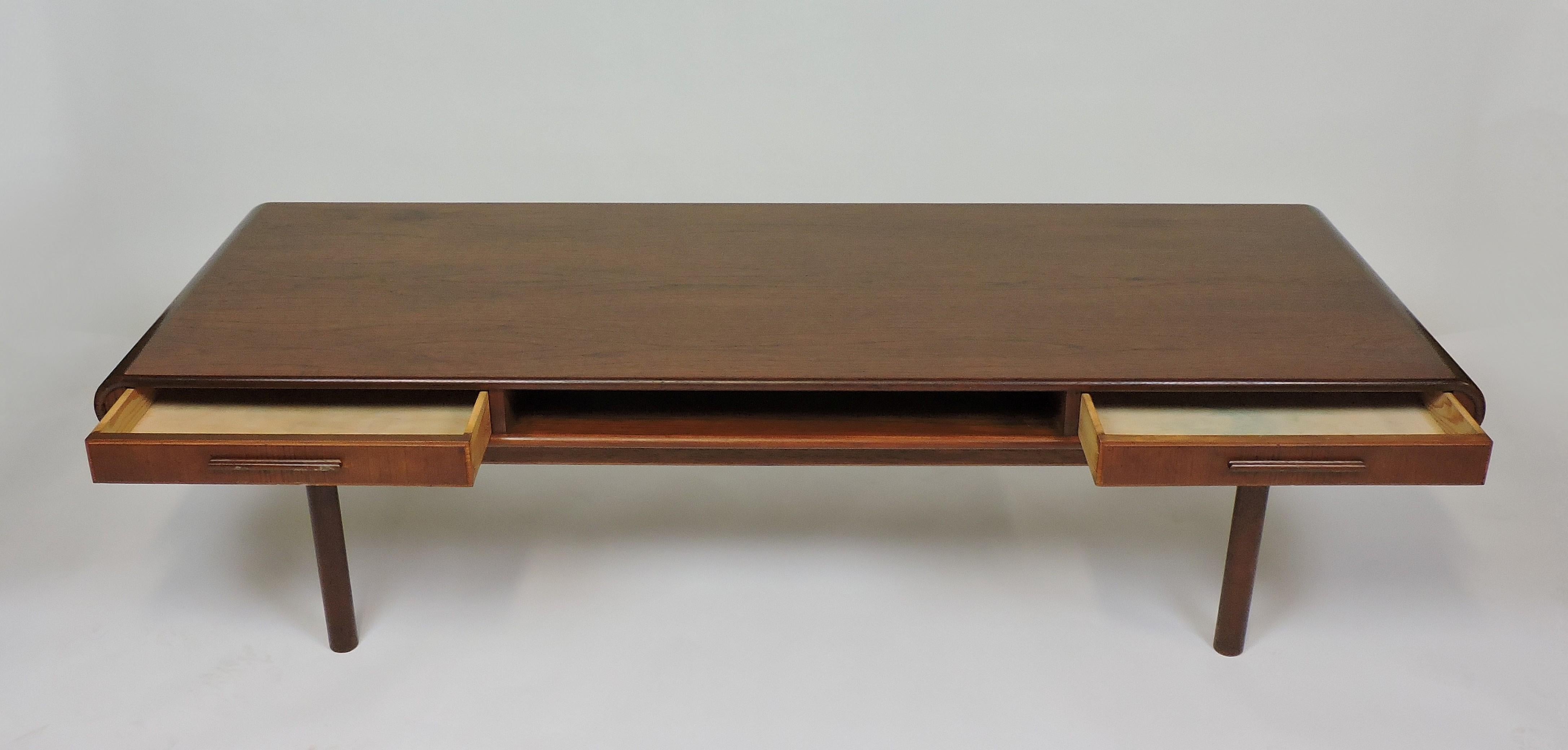 Handsome and unique Danish teak coffee table made in Denmark by Toften Mobelfabrik. This table has an enclosed shelf in the center flanked by two drawers that can be opened from either side. Clean lines and a rounded edge give this table a timeless