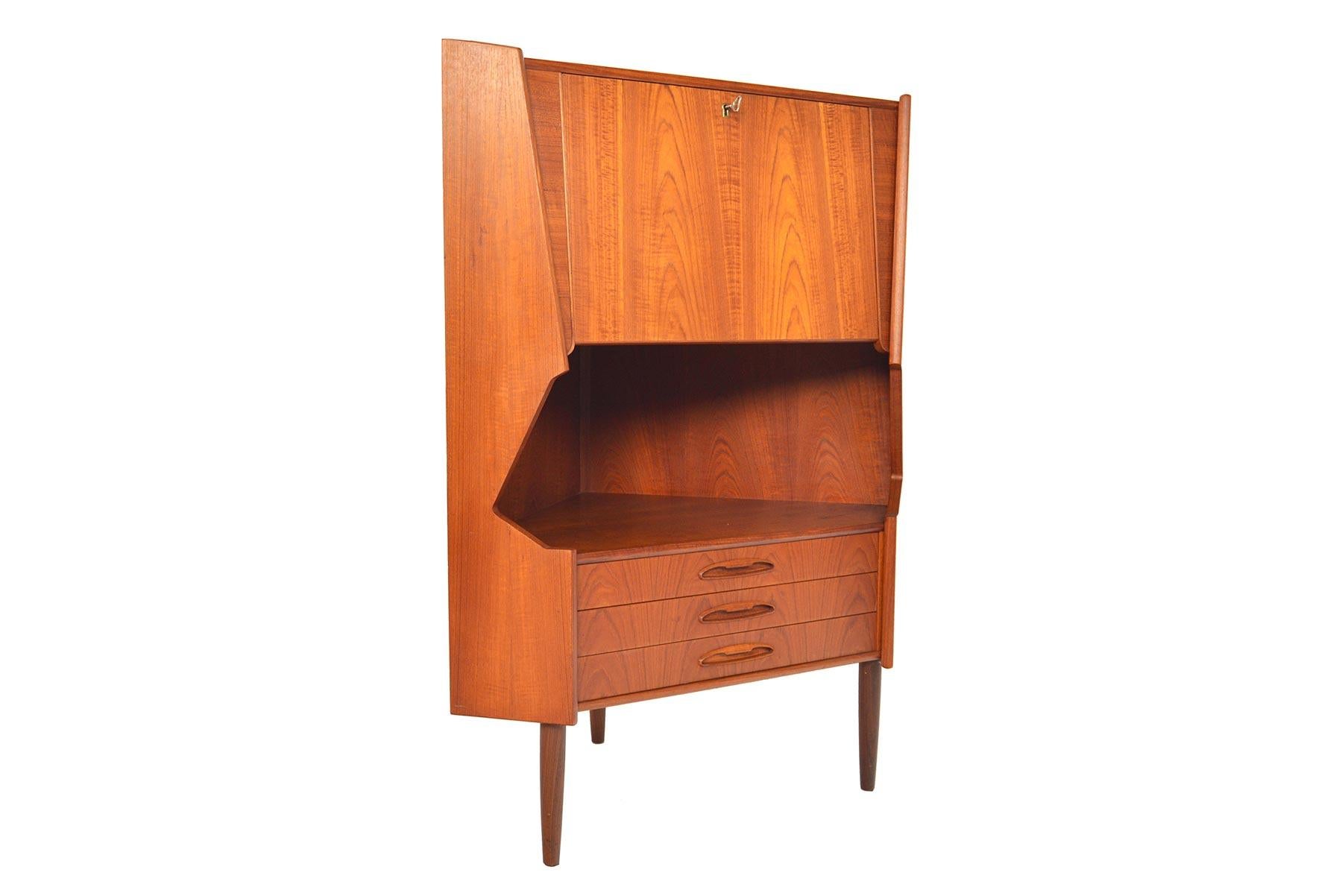 This Danish modern midcentury corner unit offers stunning bar storage. The top compartment is actuated by a key and reveals an etched mirror interior with fixed shelf. A lower cubby is perfect for bottle storage and three small drawers provide