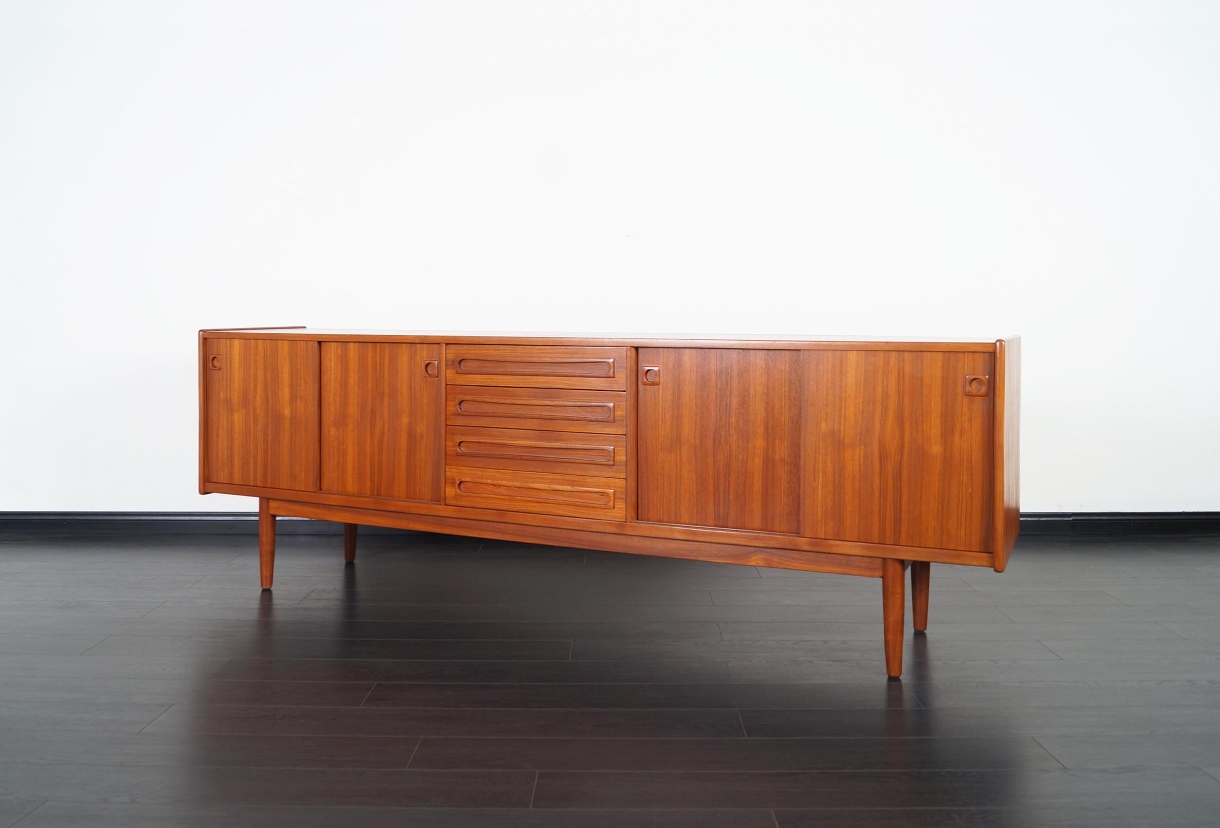 Danish modern teak credenza designed by Johannes Andersen for Skaaning Mobler. Features sliding doors with adjustable shelves on each end. The middle section of the piece has a series of four pull-out drawers for additional storage.