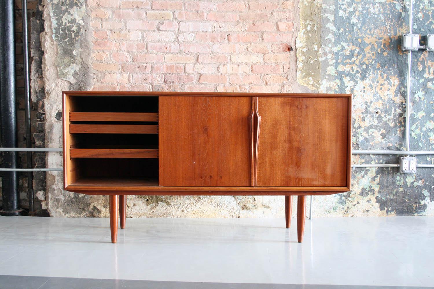 This vintage teak credenza combines Mid-Century Modern style with spacious storage options. Sliding doors hide shelves and feature elegantly carved wood handles.