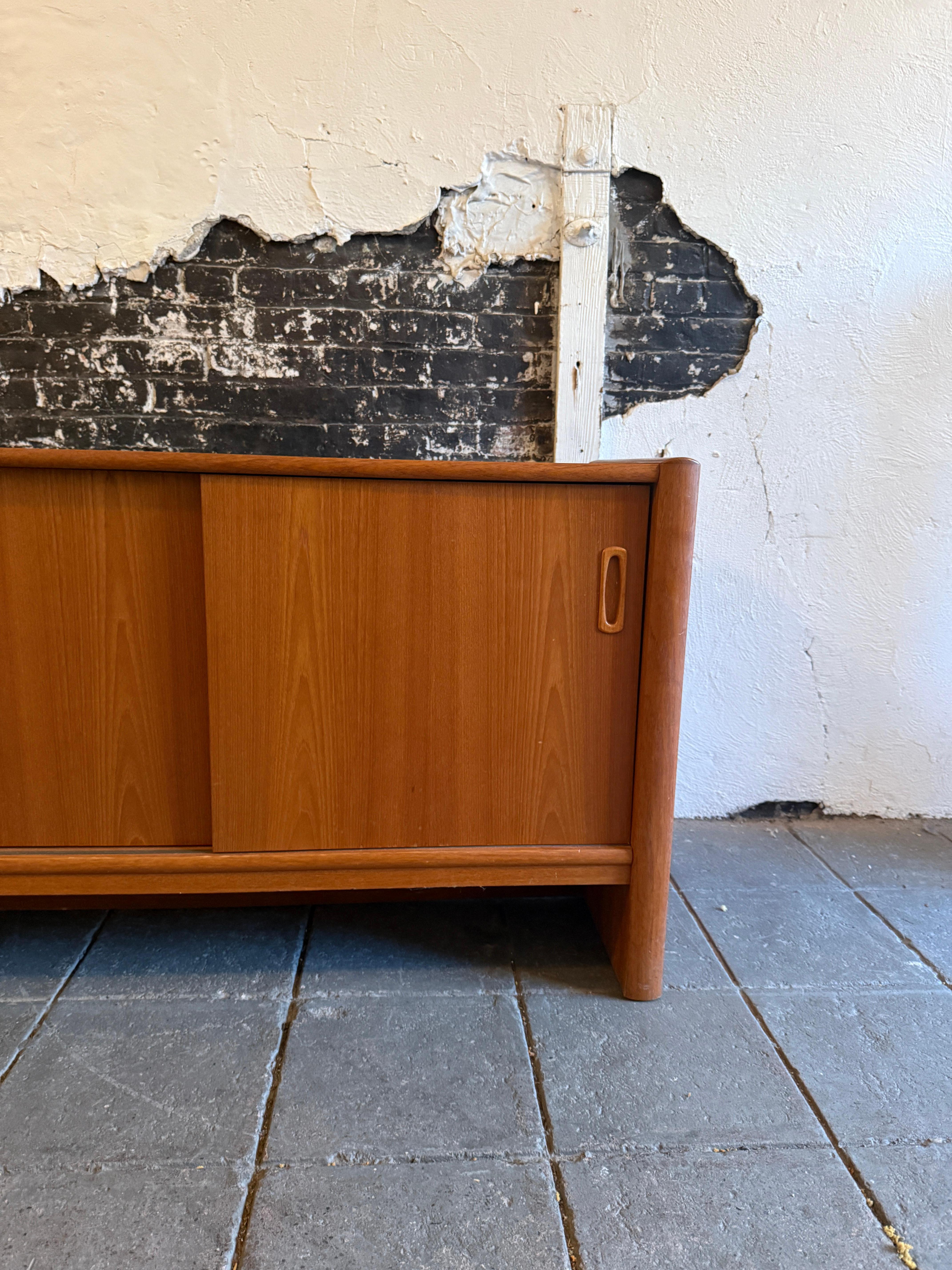 Credenza moderna danese in teak con 3 ante scorrevoli e (2) cassetti rivestiti in feltro con scaffali interni. Un bel teak chiaro e un moderno design danese. Ha maniglie intagliate a incasso su tutte e tre le porte scorrevoli. Pulito in ogni sua