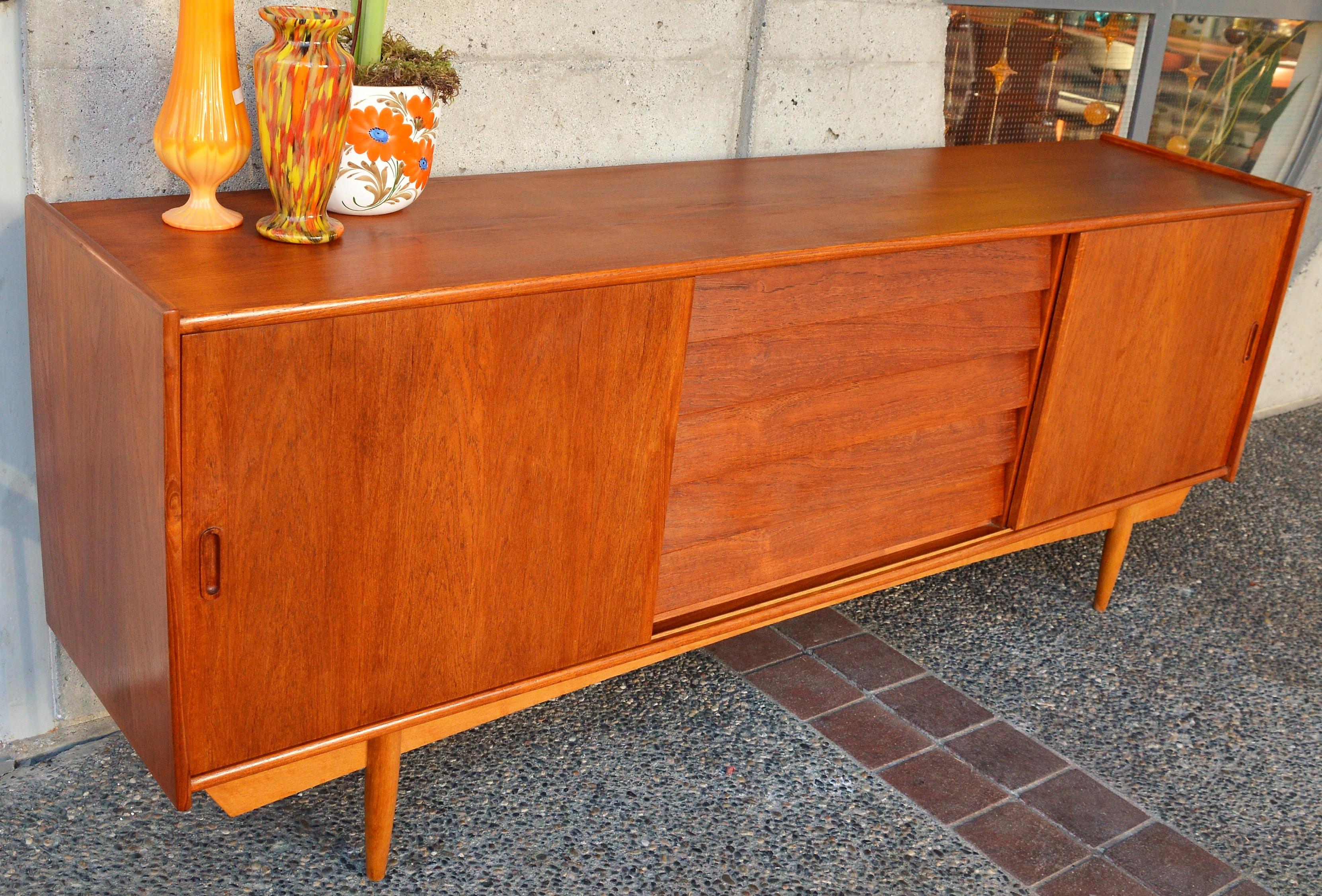 This spectacular Danish modern teak credenza buffet has a rich wonderful patina that contrasts beautifully with the sculptural oak base apron and conical legs. The centre bank of drawers are all wood frame construction with dovetail joints and have