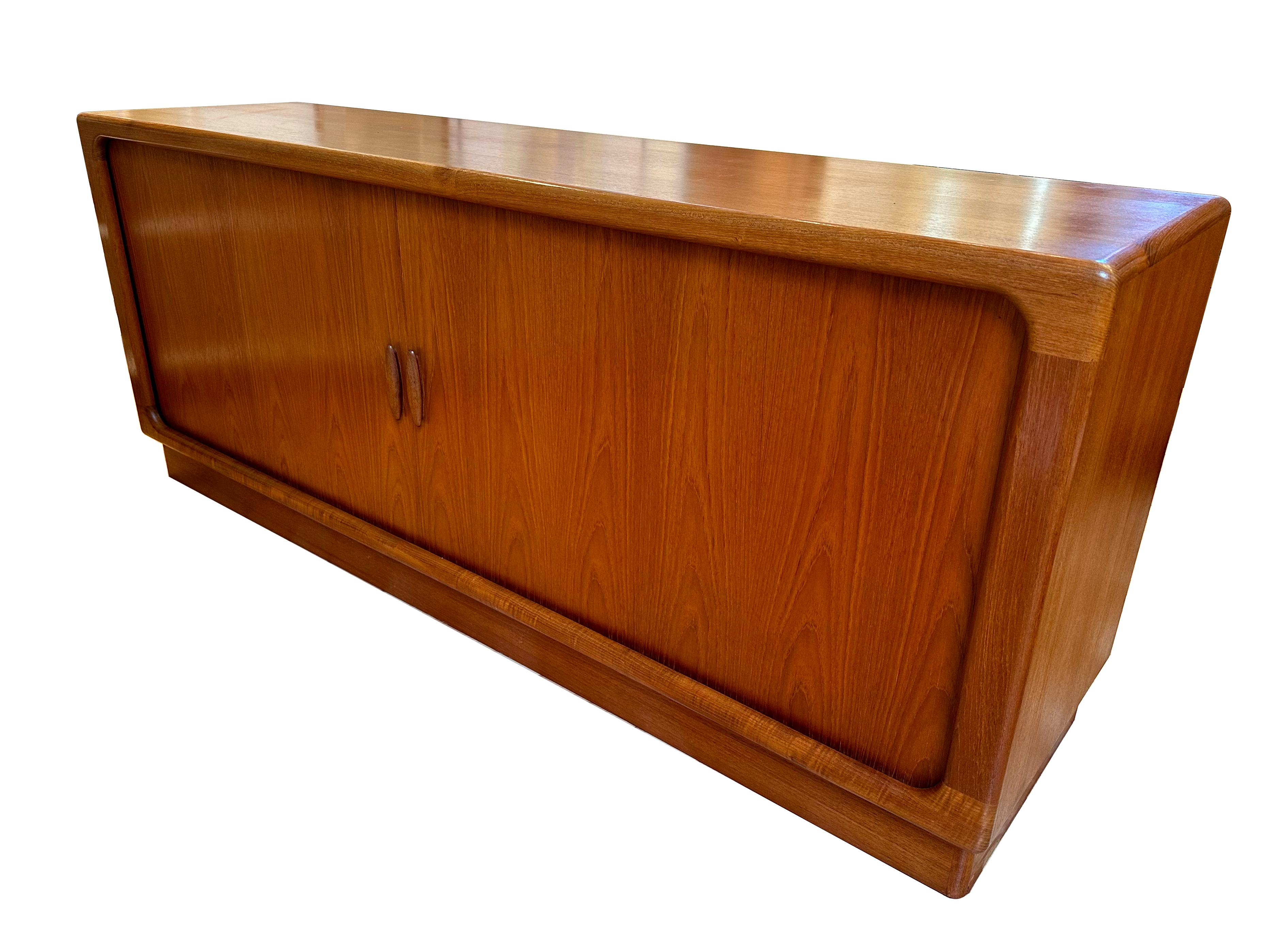 Danish Modern teak credenza by Dyrlund. The credenza has sliding tambour doors and turned teak pulls, and has three adjustable shelves and five drawers, with a felt-lined top drawer. In excellent condition, though there is some veneer damage to the