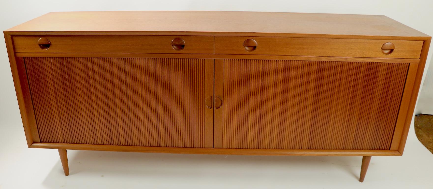 Classic Danish modern teak credenza with two upper drawers over a tambour roll front, which opens to shelved storage. Designed by Poul Dinesen made in Denmark, very good original condition, a later hole was created bottom left case see pictures,