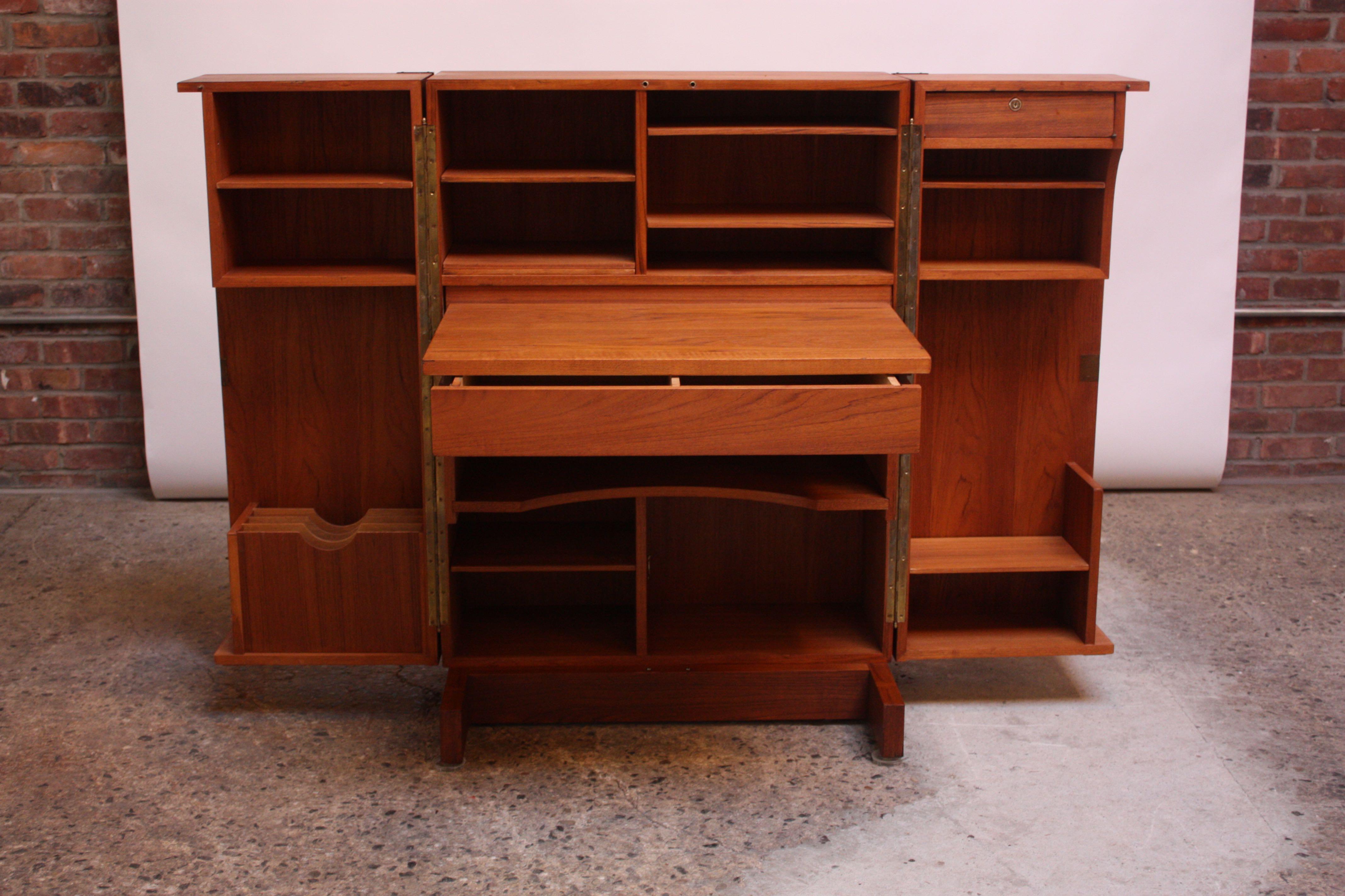 Ingeniously designed Danish modern teak cabinet finished with brass corners, whose hinged doors open to reveal a full work station. Features a slide out desk top / work surface with drawer underneath, multiple shelves / storage cubbies, a filing