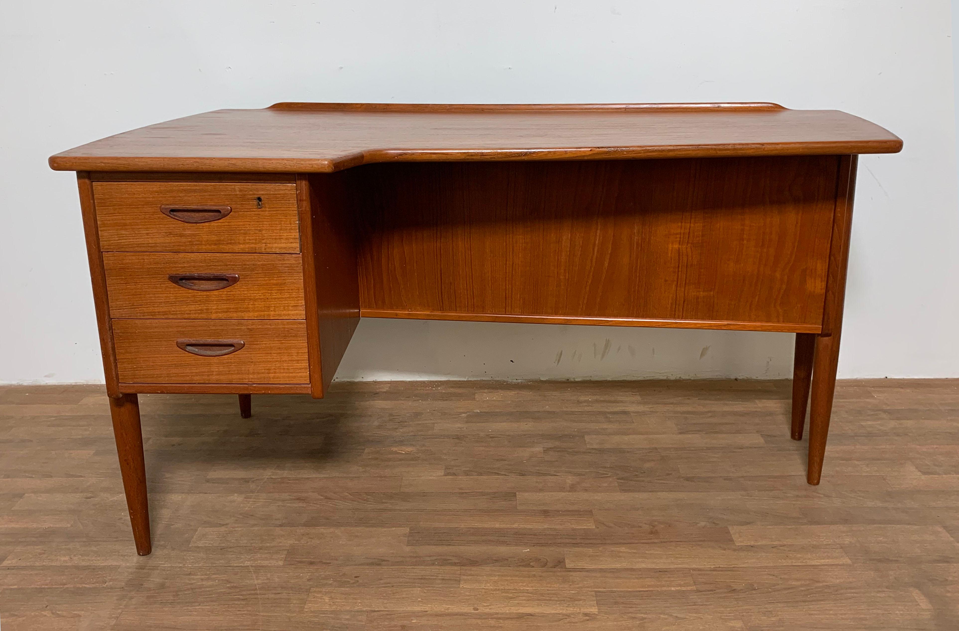 Teak desk with an asymmetrical top designed by Göran Strand for Lelångs Möbelfabrik, Sweden in the 1960s. Features a bookcase back and locked drop down storage area. Measures 29