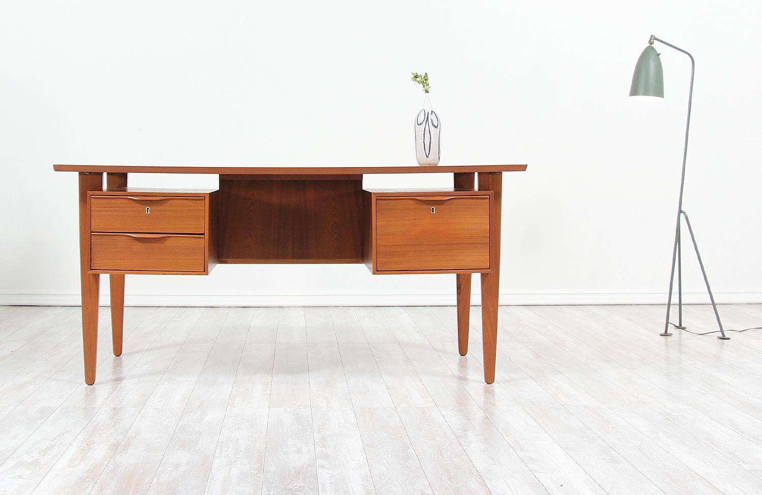 Elegant Danish modern desk designed and manufactured in Denmark, circa 1960s. This double-sided desk features a teak wood frame with three front drawers with sculpted handles and an open back with three compartments for optimal storage and many