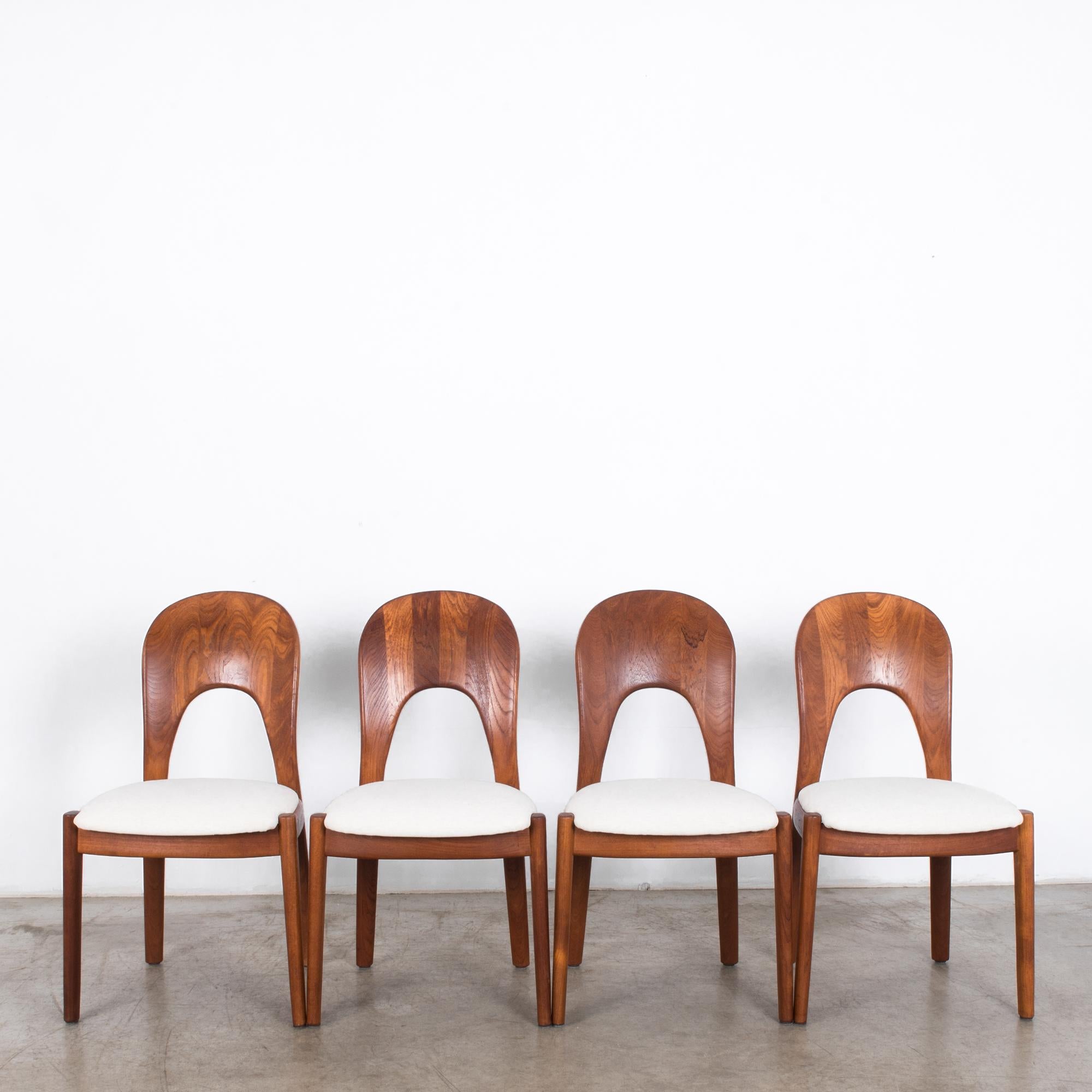 A set of four teak dining chairs from Denmark, circa 1970. Smooth curves and rounded forms speak to Scandinavian modernism, while a spoon-backed silhouette and a cushioned seat echo classic dining chair design. Reupholstered in a natural white
