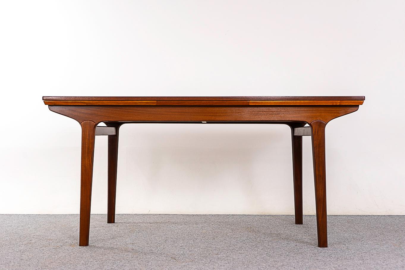 Teak dining table by Johannes Andersen, circa 1960's. Top is framed in solid wood edge trim, center panels feature highly figured veneer with book-matched grain. Self-storing leaves slide out from each end, extending the table surface by nearly two