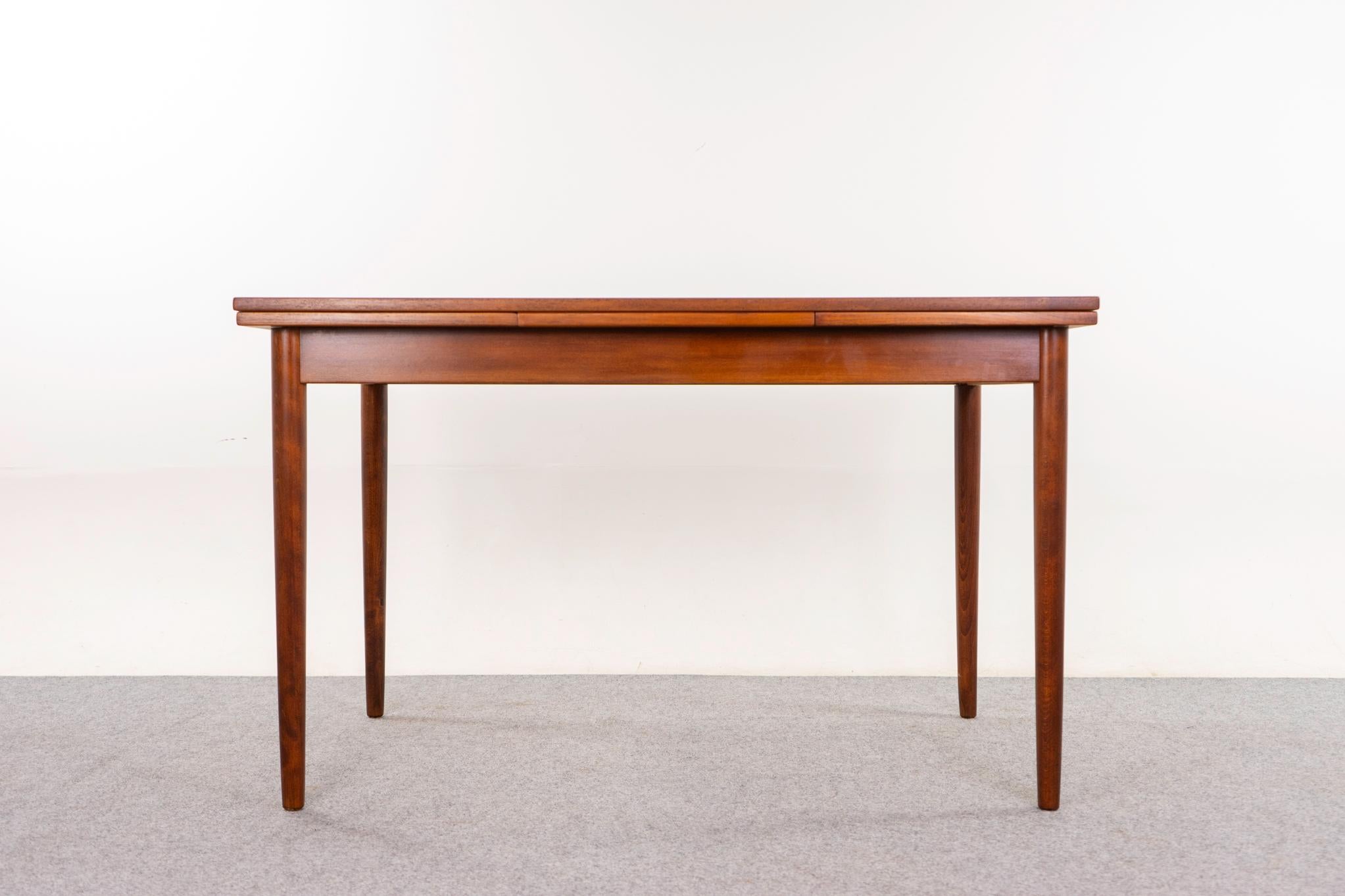 Tavolo da pranzo danese in teak, anni '60 circa. Il piano è incorniciato da un bordo in legno massiccio, mentre i pannelli centrali sono caratterizzati da un'impiallacciatura altamente figurativa con venature abbinate al libro. Le foglie
