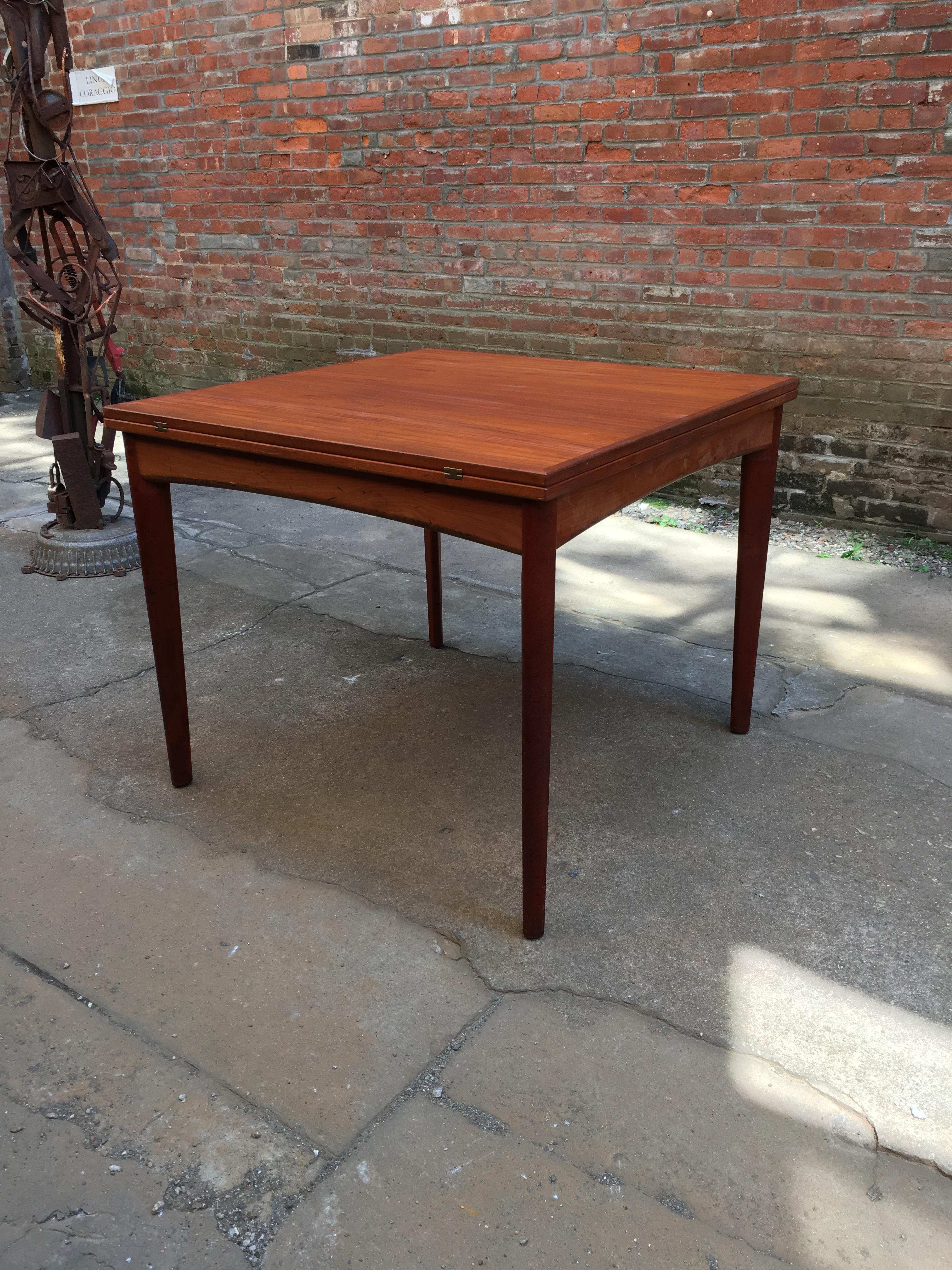 Nice square compact Danish design until you flip and slide the table top to extend it to proper dining/banquet table size. Beautifully figured teak veneers with solid teak legs and arched apron. Felted interior for hidden storage for table clothes,