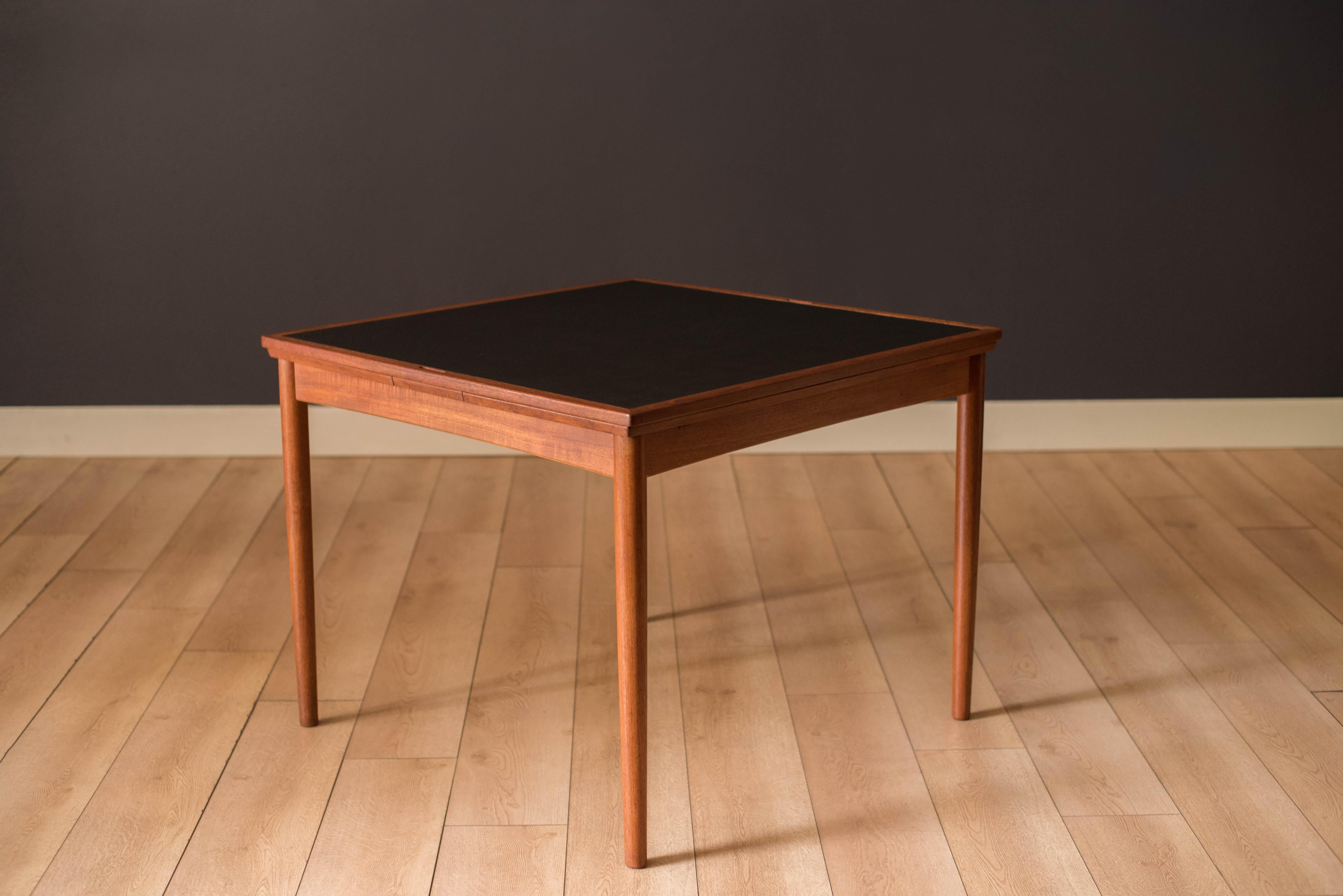 Mid Century Modern flip top card game table in teak by Carlo Jensen for Hundevad & Co., Denmark. This versatile piece has a reversible teak and black vinyl top that functions as a poker table and dining table. Seats four chairs comfortably and