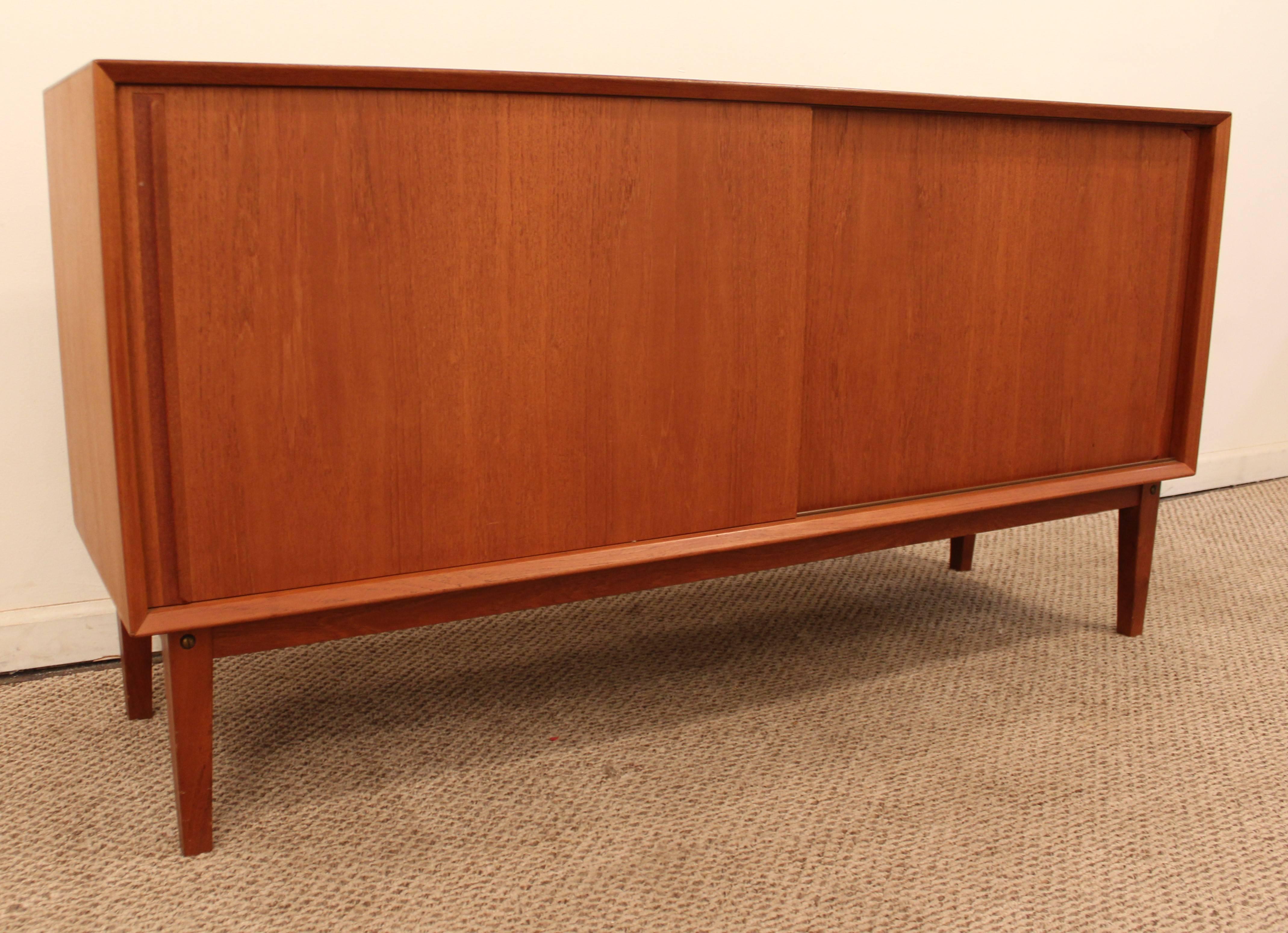 Offered is a 2-piece teak credenza (top comes off base), featuring sliding doors with shelving and drawers inside, and a floating base. 