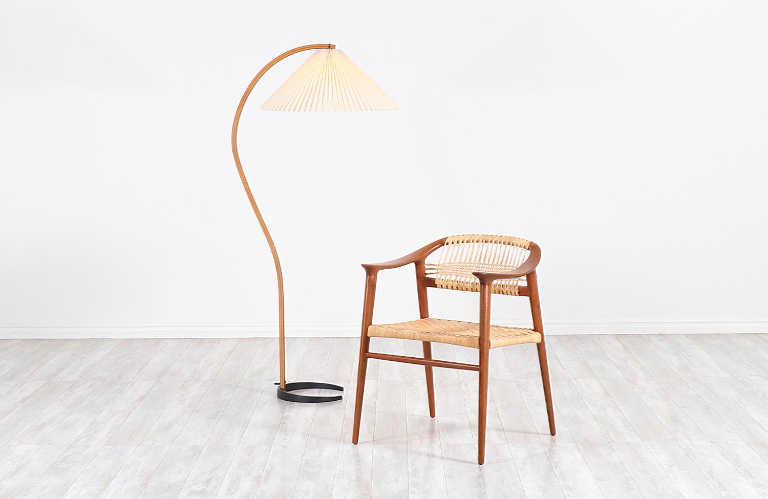 Sculptural teak floor lamp designed and manufactured by Mads Caprani in Denmark circa 1970s. This iconic Danish Modern design features a solid crescent-shaped iron base that supports the bentwood teak arm and the original pleated shade in pristine