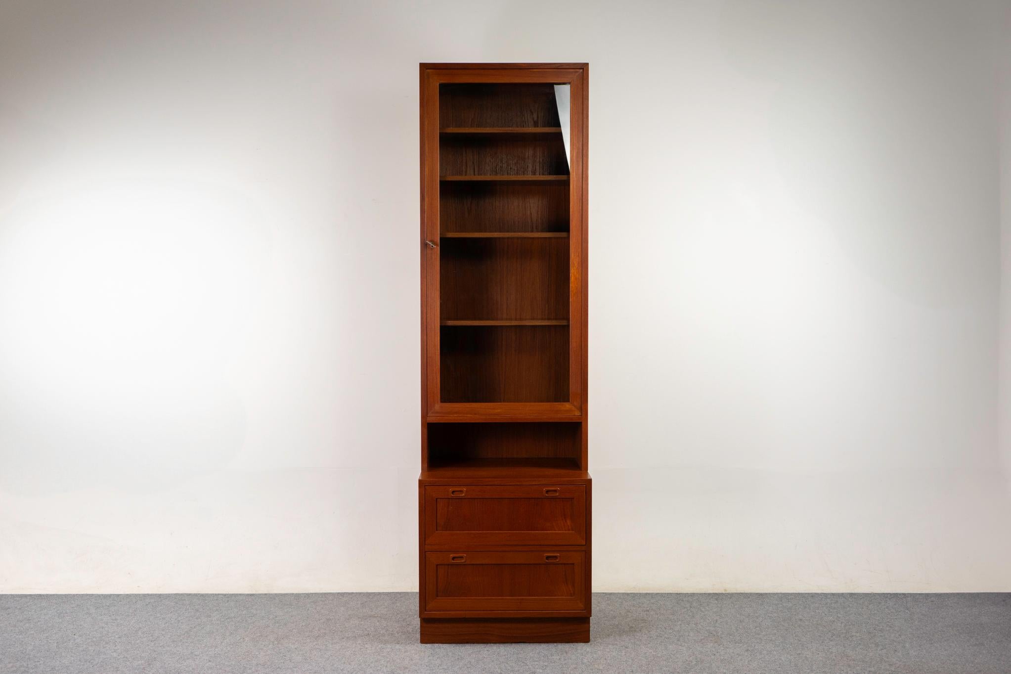Mueble danés de teca y cristal, hacia 1960. Preciosa chapa de madera a juego con el libro, de tono intenso. El armario tiene una puerta de cristal con cerradura y 4 estantes ajustables (de recambio). La sección de almacenamiento inferior descansa