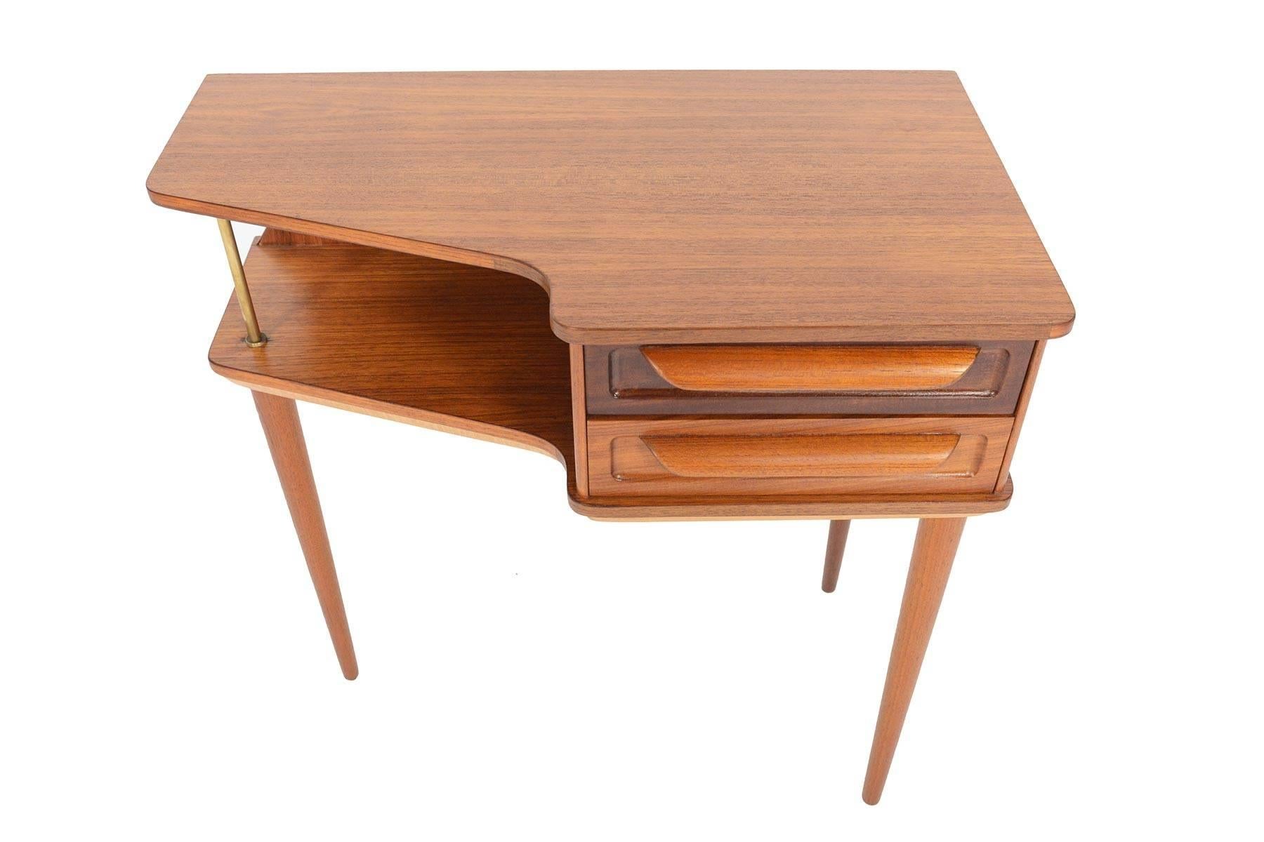 This Danish modern hallway chest offers an unusual design with a dynamic case shape and three leg design. The cabinet houses two drawers with carved pulls. The open cubby is supported by a brass rod. Stunning from every angle, the table top and back