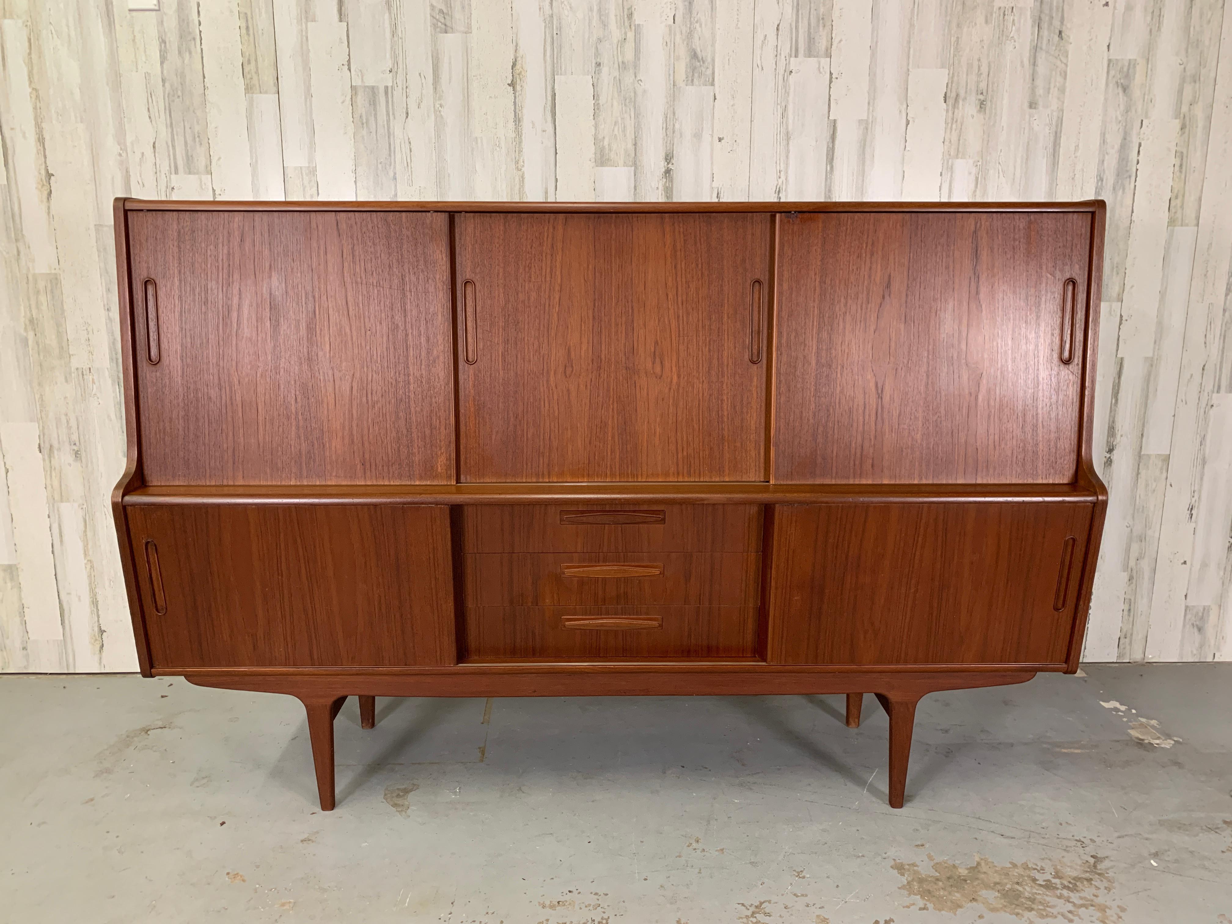 Danish Modern Teak High Board. Sleek sliding doors with sculpted handles. Shelves are inside of the sliding doors for tons of storage space. Can also be used as a dry bar.