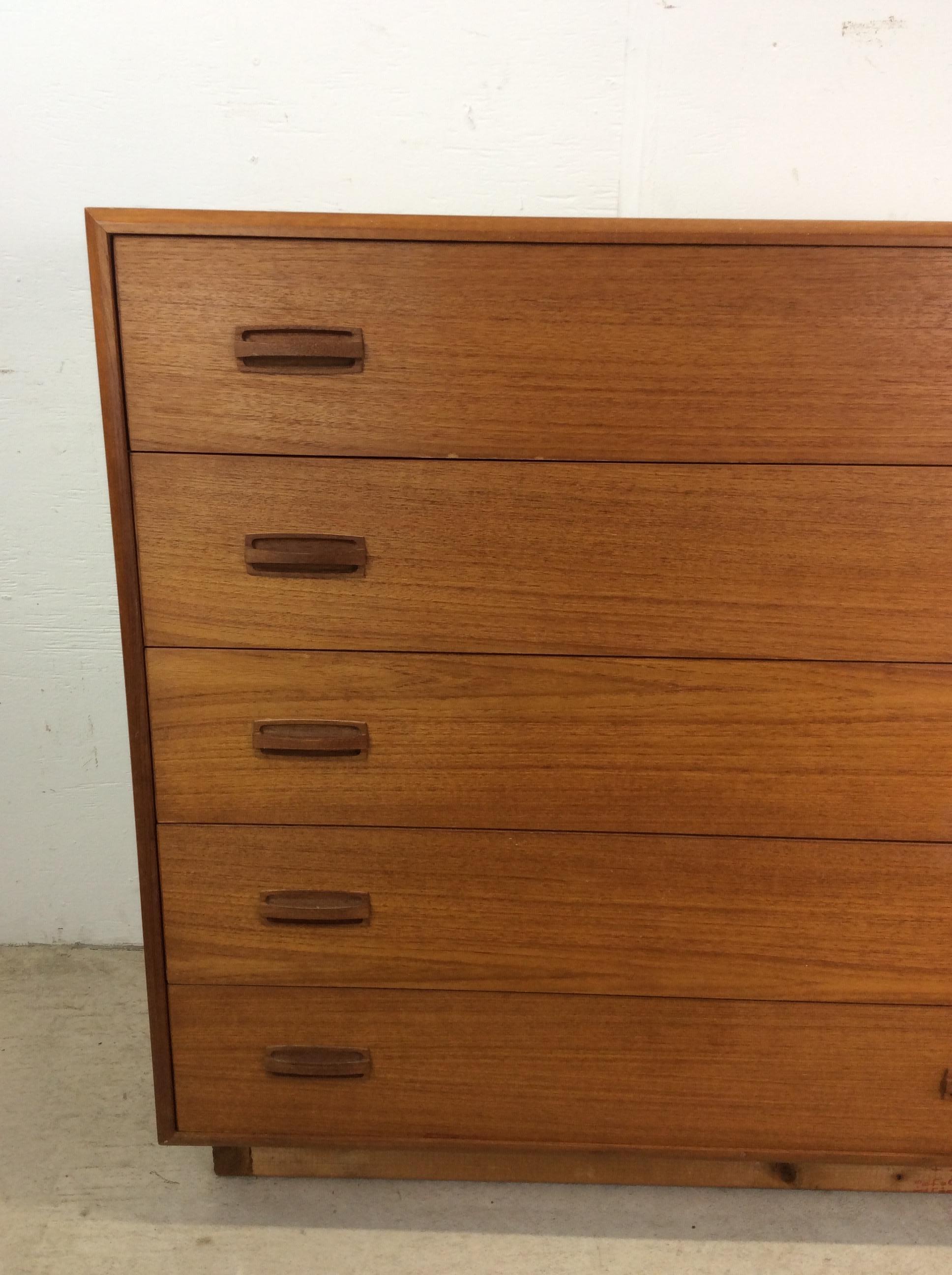 This Danish modern highboy dresser features pressed wood construction, teak veneer with original finish, five drawers with wood pulls, and wooden plinth base.  Matching highboy dresser with mounted mirror, nightstand, and bed frame with storage