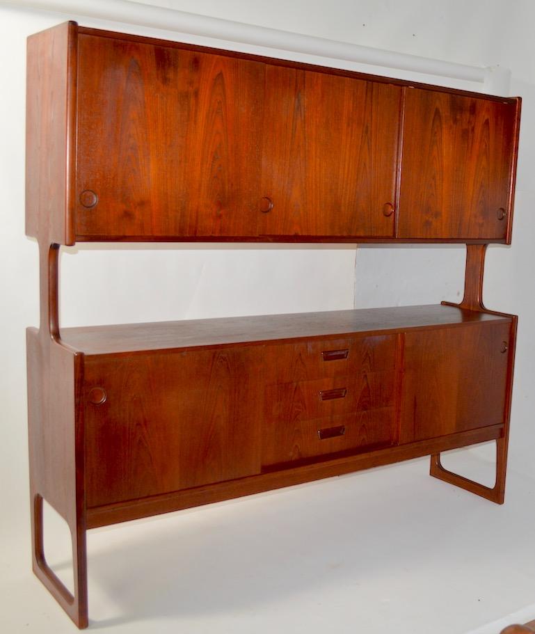 Very nice Danish modern sideboard in richly grained teak. The top has three sliding doors, one opens to interior drawers, the other two open to shelved storage. The bottom has sliding doors, which open to shelved storage, and drawers in the centre.