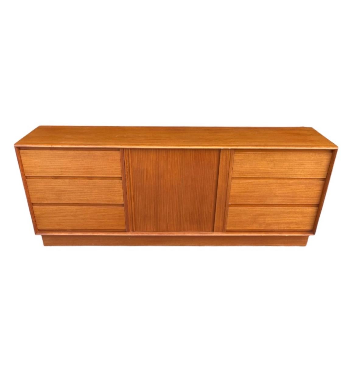 Handsome and elegant Danish modern long dresser in teak. Versatile enough to be used as a credenza or media center. Symmetric form with drawers on both ends with vanishing tambour door in the middle to reveal ample storage space. Beautiful color and