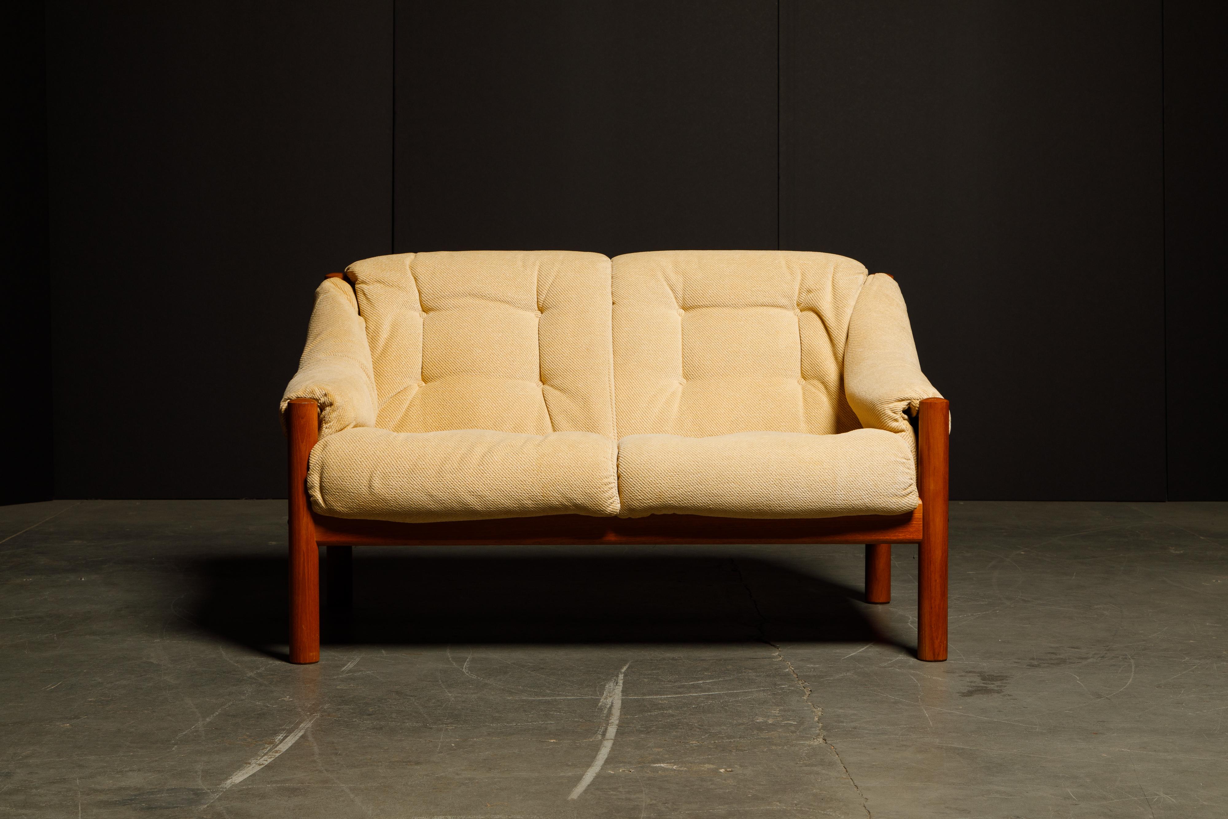This Danish Mid-Century Modern loveseat from Domino Møbler, was made in the 1970's in Denmark. Featuring sculpted arms with a solid teak frame and cylindrical legs, with tufted cushions upholstered in its original fabric, making this sofa just as