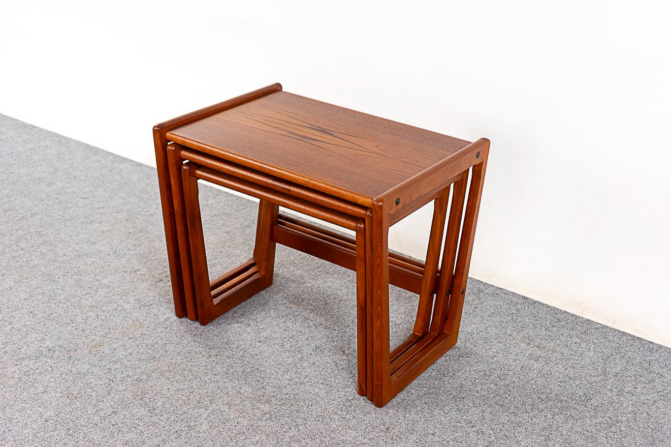 Teak mid-century nesting tables, circa 1970's. Striking solid teak trapezoidal legs and bookmatched veneer tops.The footprint of 1 table with the functionality of 3!  Top of the middle table has minor sun fade.