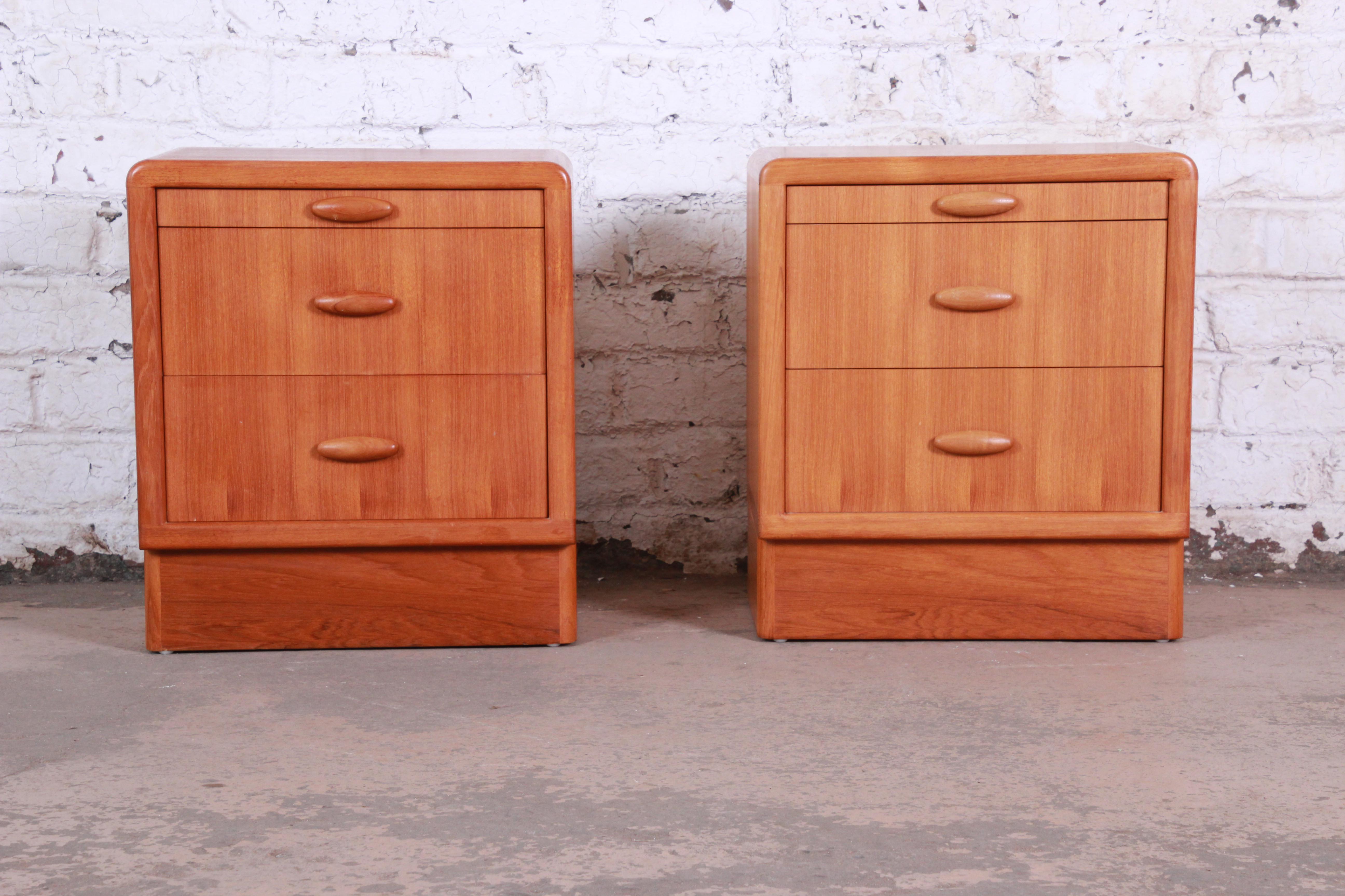 A gorgeous pair of Danish modern teak nightstands by Dyrlund. The nightstands feature stunning teak wood grain and sleek midcentury Danish design. The offer good storage, each with two drawers and a pull-out writing tablet. The sculpted solid teak