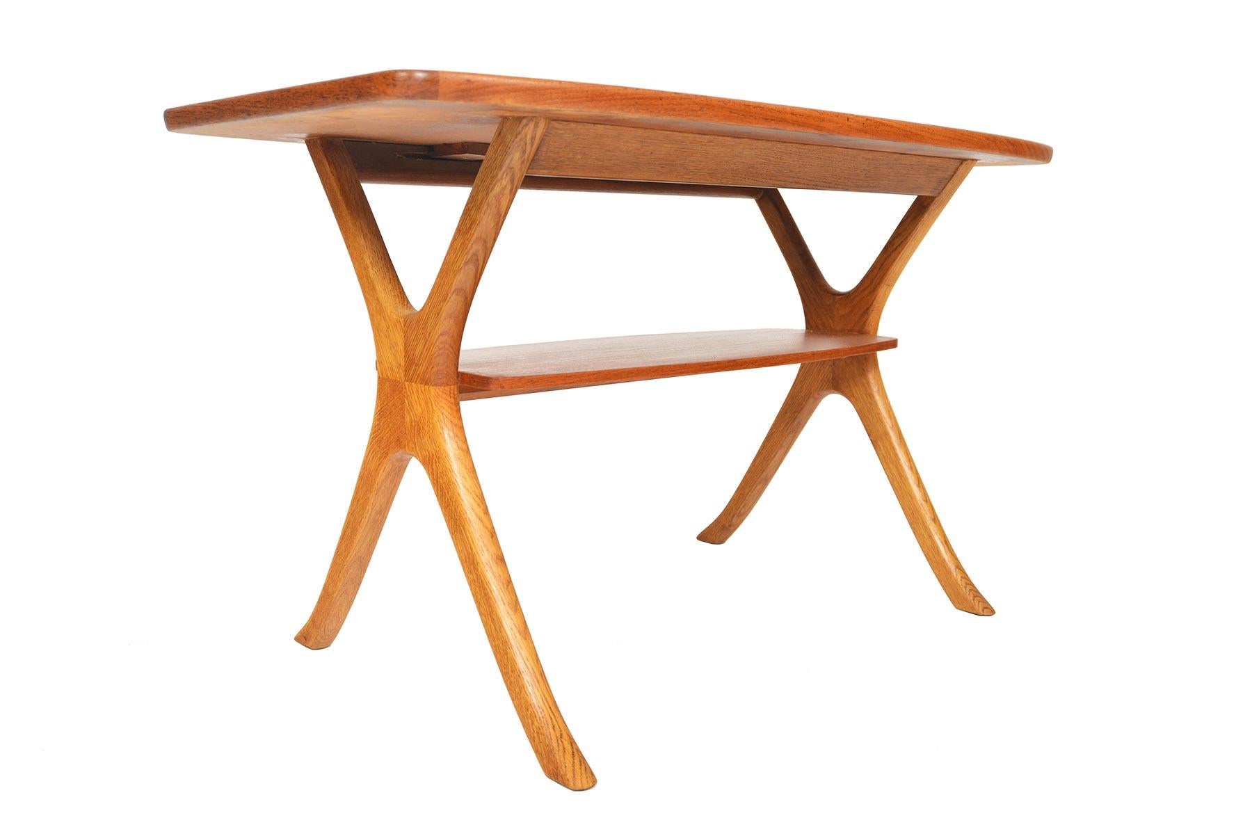 This Danish modern teak and oak coffee table offers a beautiful organic form. A raised lip runs the banding of the teak table top. Solid oak legs feature unique joinery and support a lower teak shelf. In excellent original condition.