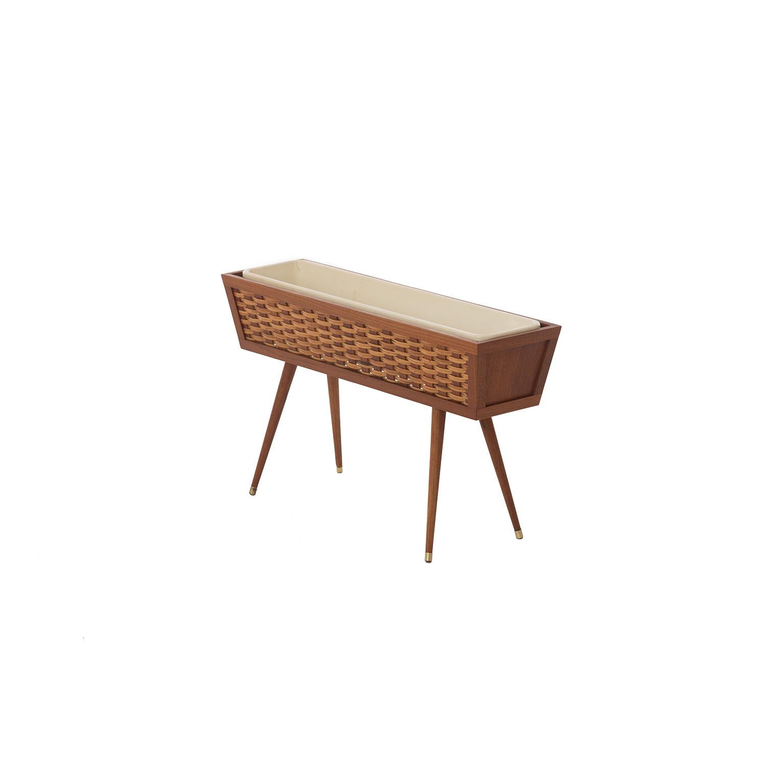 This petite teak planter has woven cane and teak detailing along the sides and brass ferrules on the feet. Angled legs and sides add midcentury flair. Liner is old fashioned plastic, perfect for setting in pots. Rosebud motel eat your heart out. A