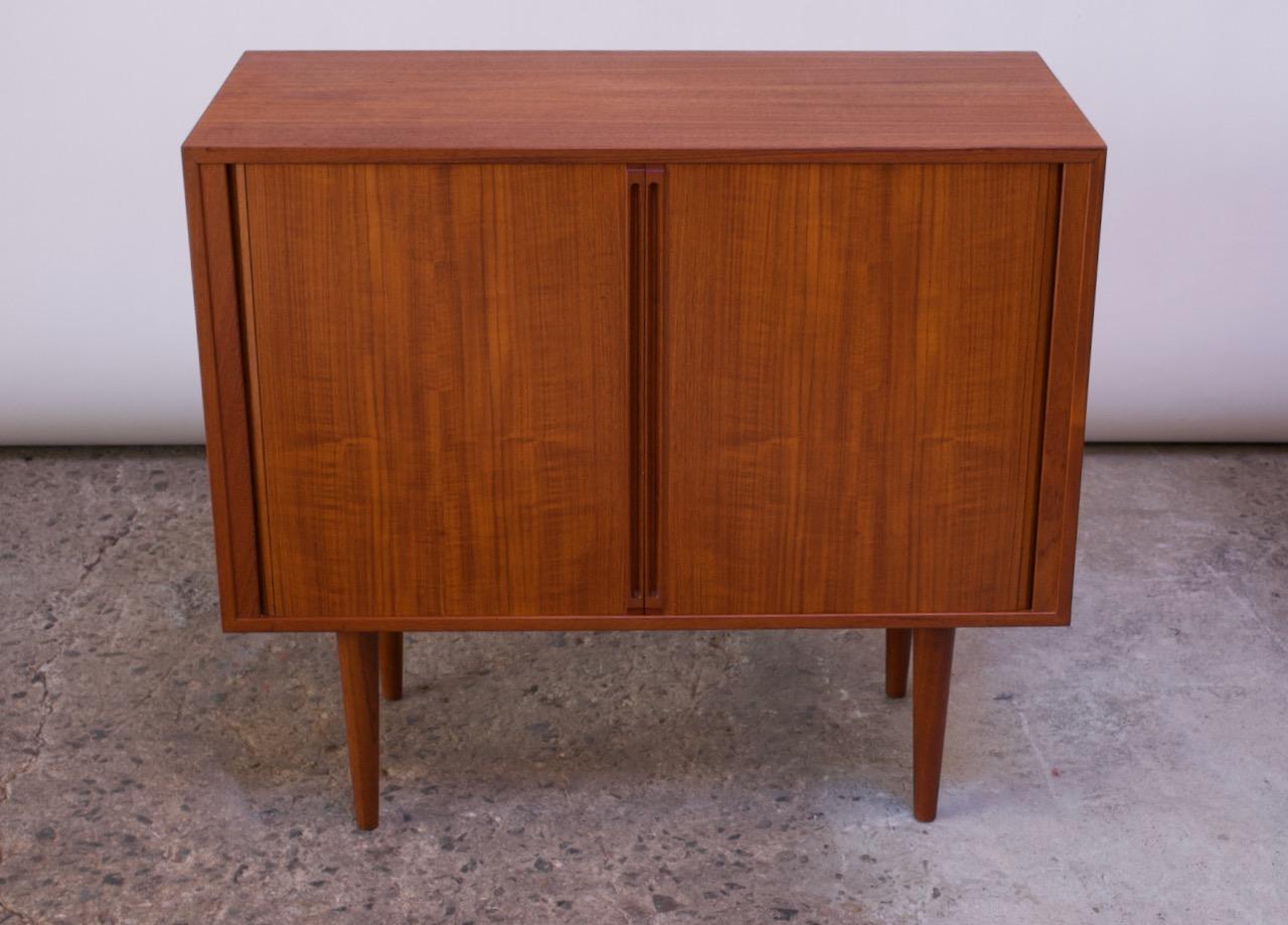 Stylish and compact teak cabinet designed in the 1960s by Kai Kristiansen for Feldballes Møbelfabrik of Denmark.
The two tambour doors with elongated, recessed pulls open to reveal seven sections for records with built-in dividers above two