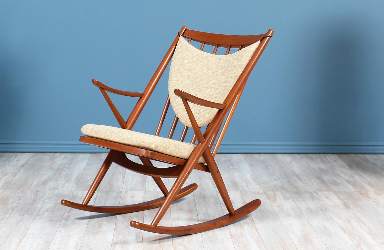 Comfortable rocking chair designed by Frank Reenskaug for Bramin Møbler in Denmark circa 1960’s. Features a teak wood frame with six vertical spindles on the open back for support. The sides, below the arm rests, feature an X-shape that connects the