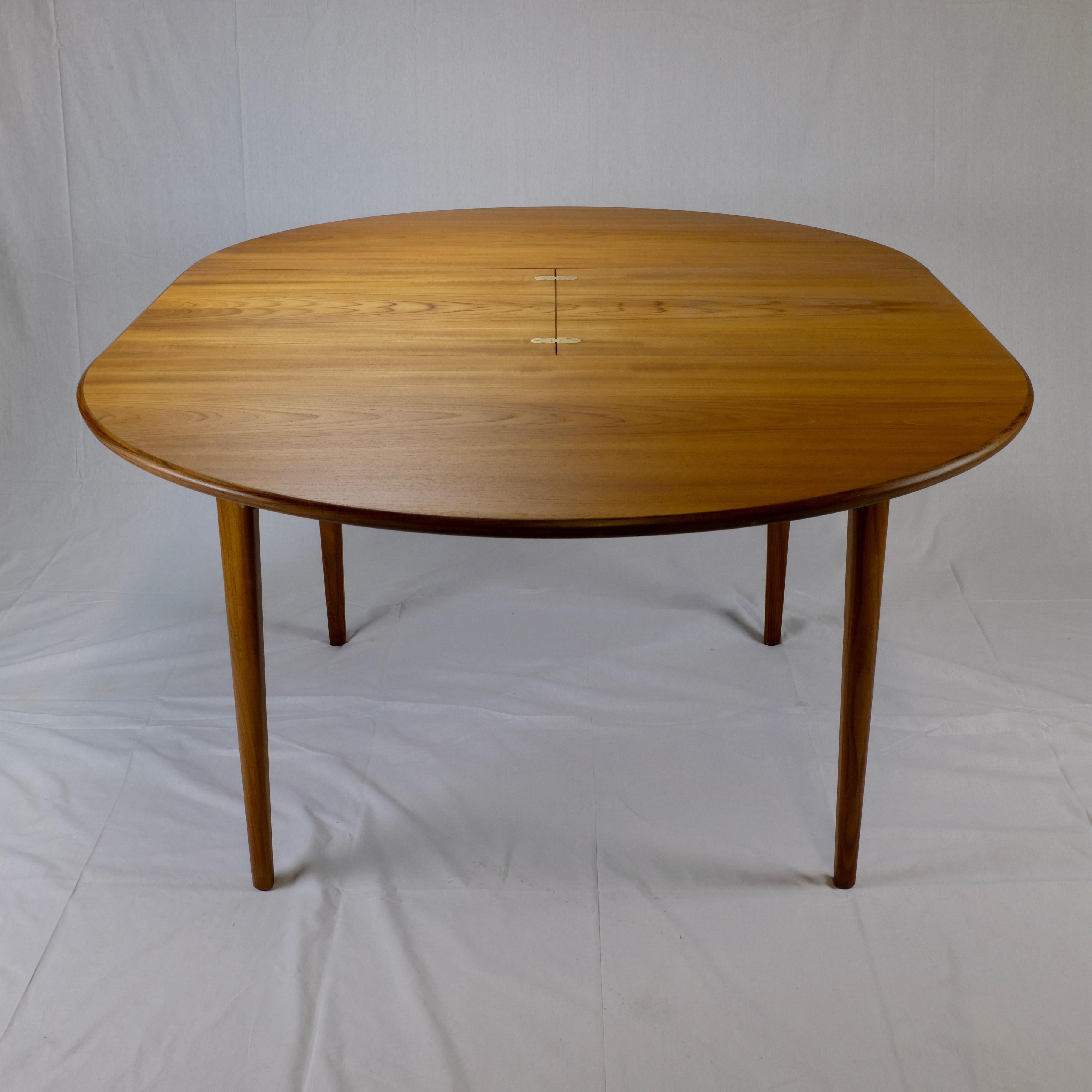 Round dining table made in Denmark featuring a butterfly extension leaf with brass flush-mounted hinges. The table measures 68.5