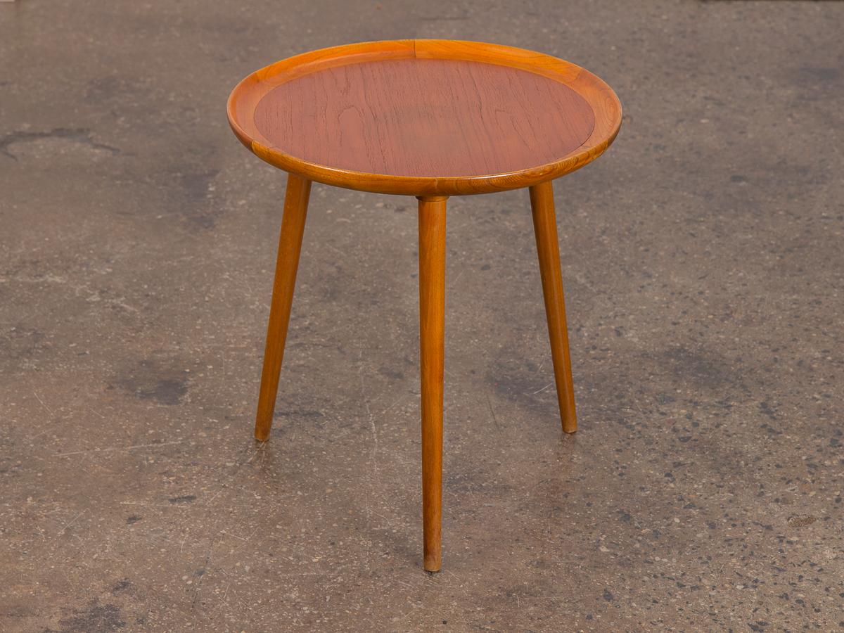 Three-legged Danish Modern teak round side table. Pretty circular table has been polished an cleaned, with a gleaming wood selection and a carved lip detail. Table is in very good condition, surface is very clean with no major rings. Delicately