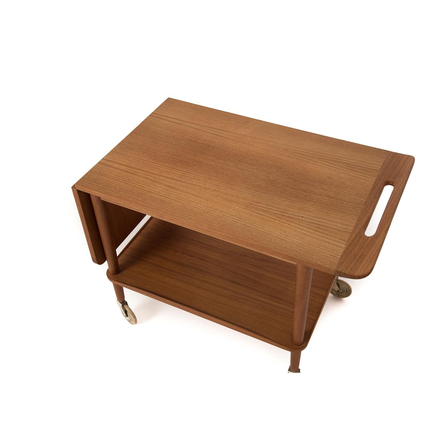 This original Danish modern serving cart is made from old growth teak, traditionally finished with oil. The top of this cart slides to the right to increase serving surface, the sculpted handhold makes the move convenient. Lower teak shelf provides