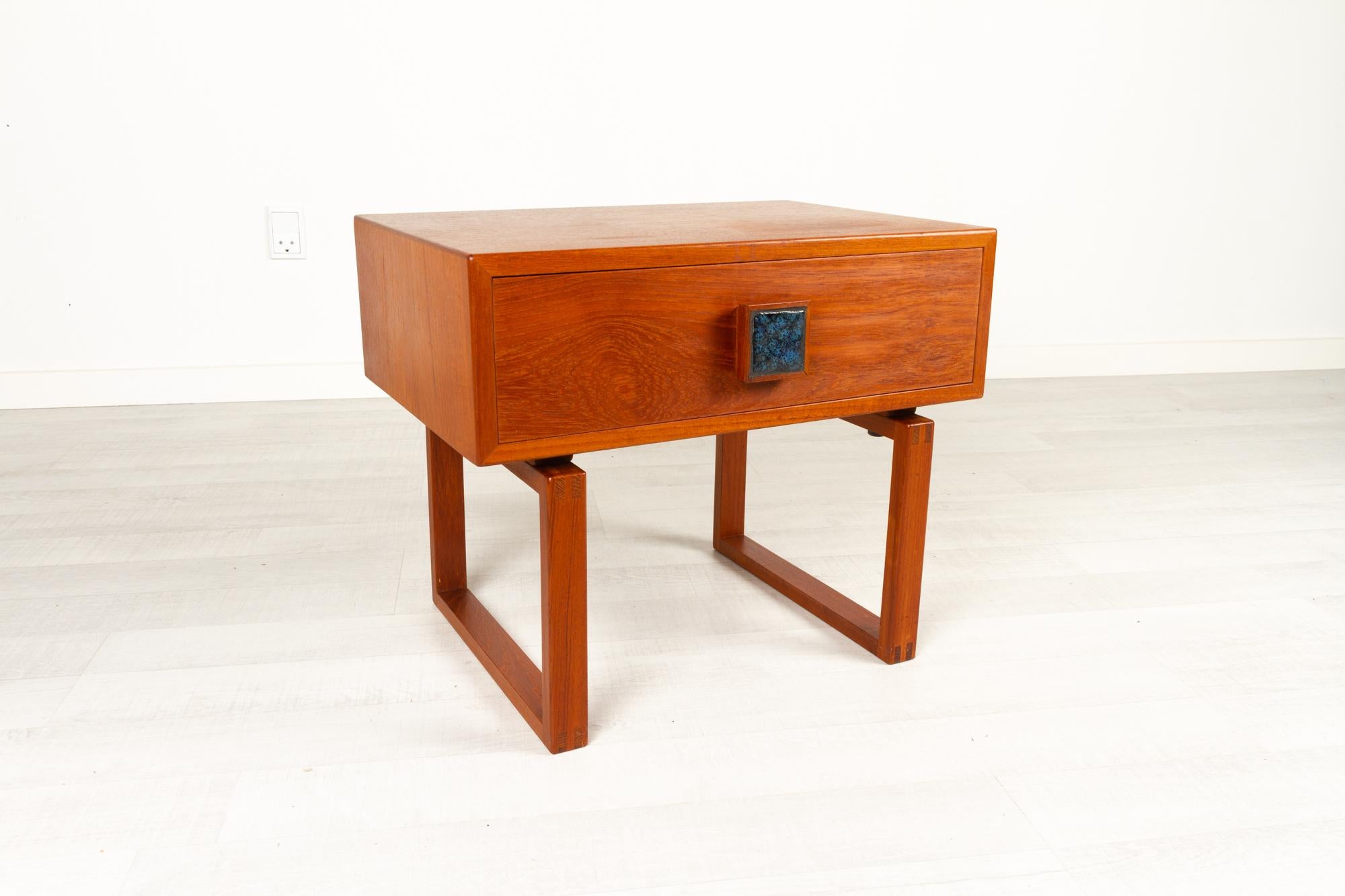 Danish modern teak side table, 1960s.
Danish Mid-Century Modern one drawer dresser with sleigh legs. Very good build quality and craftsmanship with dovetail joints. Pull in teak with a blue ceramic tile inlay. Very elegant and lovely table with