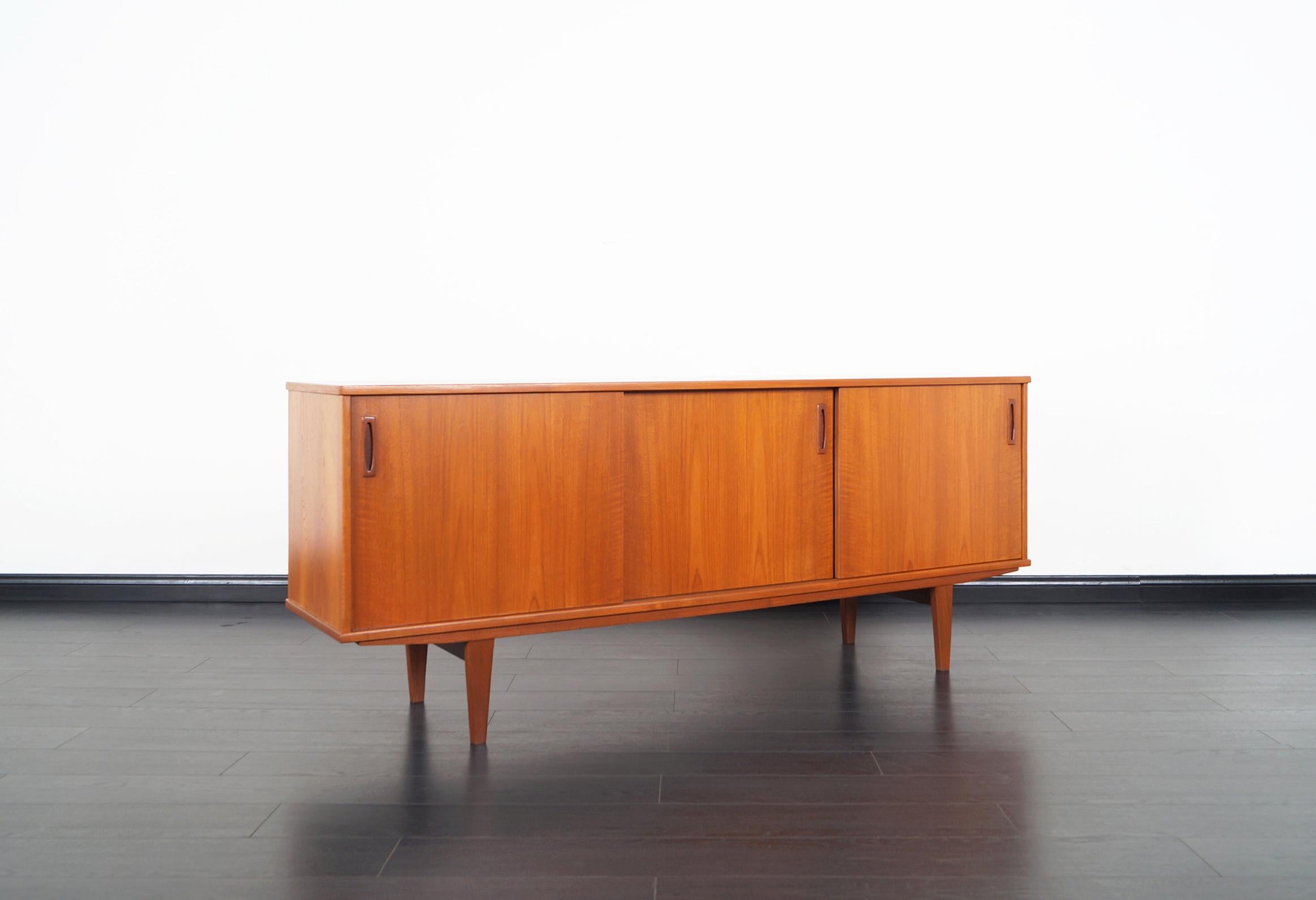 Danish modern teak sideboard manufactured by Dyrlund. Features three sliding doors that opens up to three sections. The middle and left side has one adjustable shelf each. The right side has two pull-out trays and one shelf.